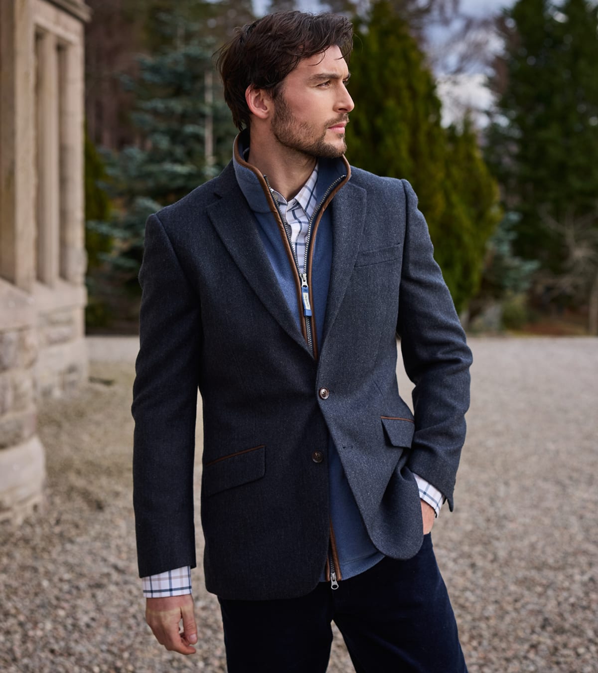 Man wearing a charcoal wool-blend blazer with brown trim over a blue overshirt and checked shirt outdoors.