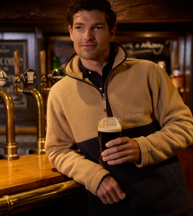 Person wearing a two‑tone retro fleece, standing indoors at a bar holding a drink.