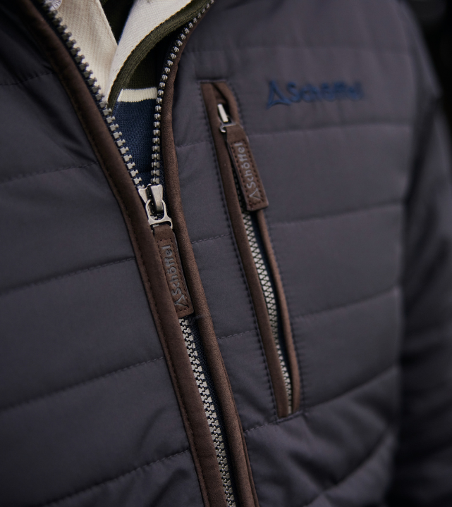 Close-up of a dark blue quilted jacket with brown zippers and a brand logo.