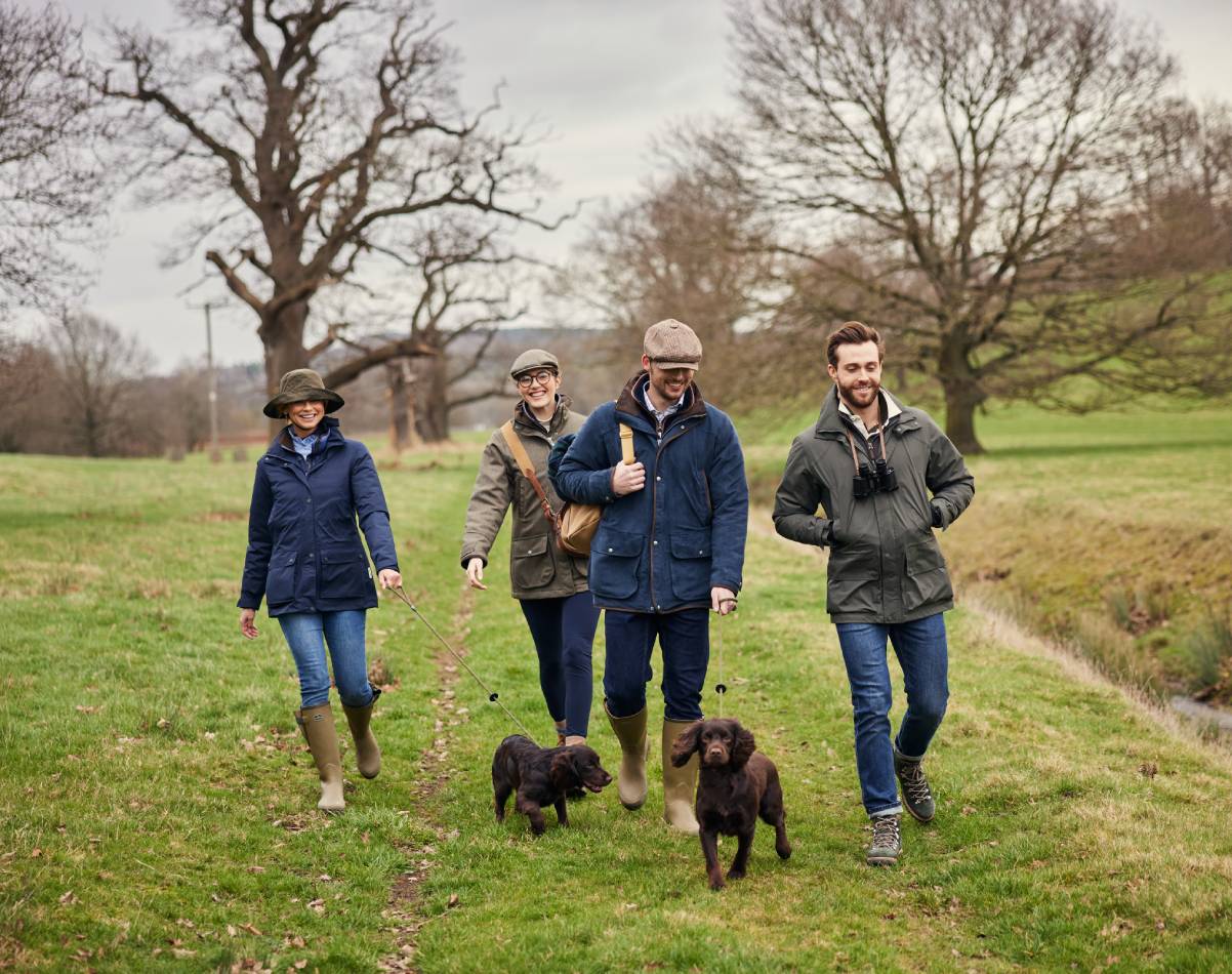 A group of people and dogs walking in a field wearing countrywear.