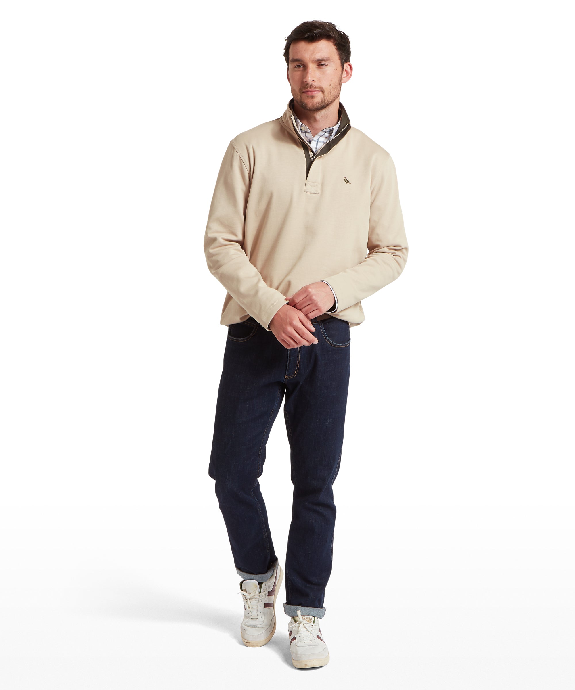 Man wearing a beige sweatshirt and navy jeans on a white background
