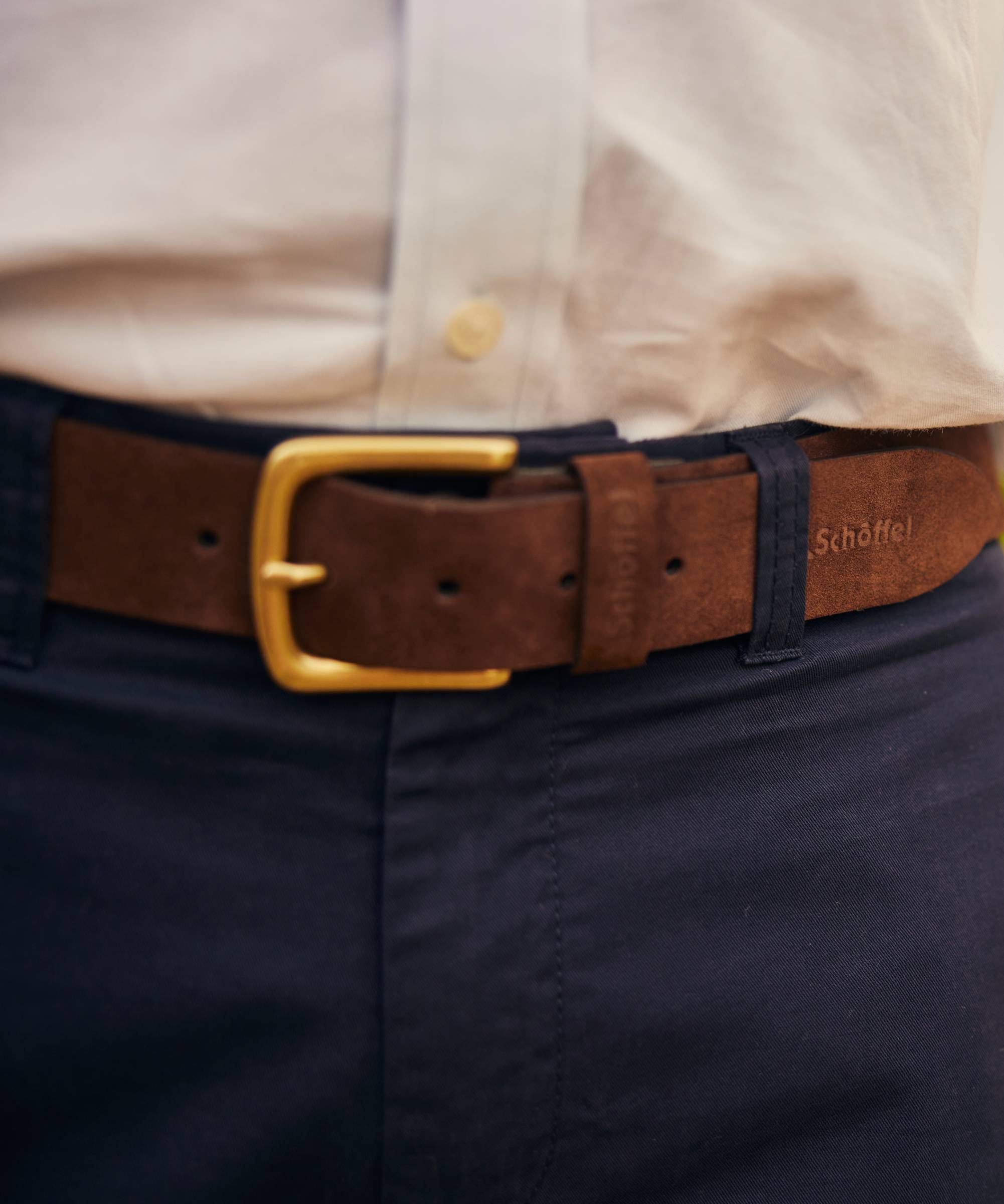 Brown belt with gold buckle on navy pants, worn with a light-coloured shirt.