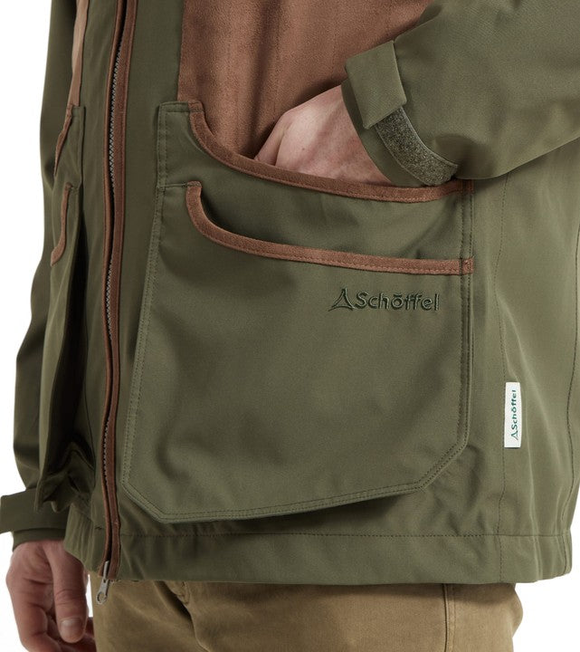 Detail of Schöffel Men's Grimsthorpe Clay Shooting Jacket in olive green, highlighting the large suede-trimmed bellows pocket with embroidered Schöffel logo and cuff adjustment