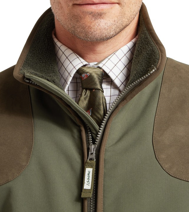 Schöffel Gunby men's jacket in green, close-up of fleece-lined collar and contrast tweed-effect shoulder patches, full-length zip with branded pull tag, styled with checked shirt and tie