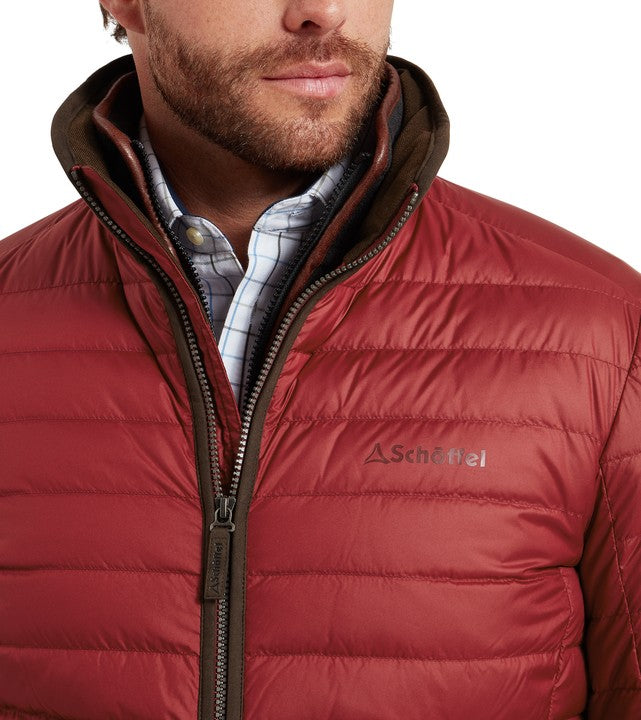 Close-up of Schöffel Men's Hallaton Down Jacket collar in deep red, showing the quilted front, full-length zip with branded pull, contrast brown trim and embroidered Schöffel logo, worn over a check shirt