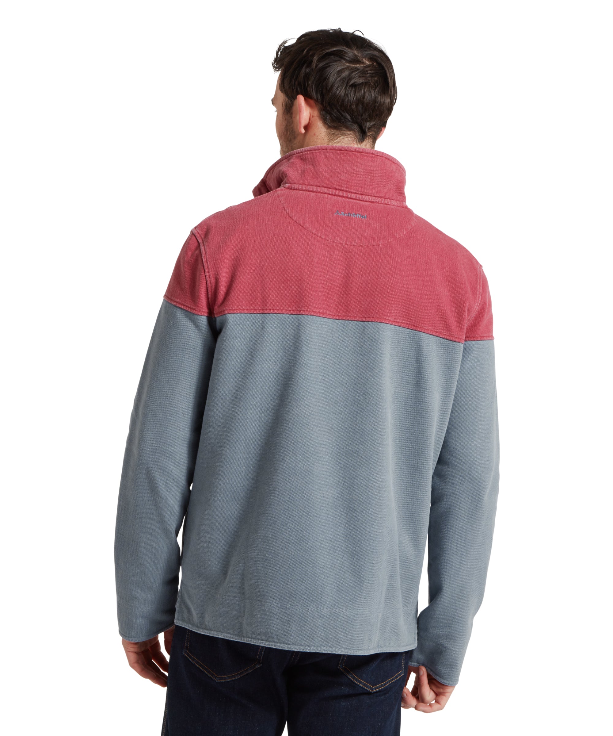 Back image of a male model wearing a blue Schöffel sweatshirt with red shoulder and chest detailing and blue 'Schöffel countrywear' logo on the chest. It is paired with a red polo and dark denim jeans. He is standing in a relaxed pose looking towards the camera with his hands by his side.