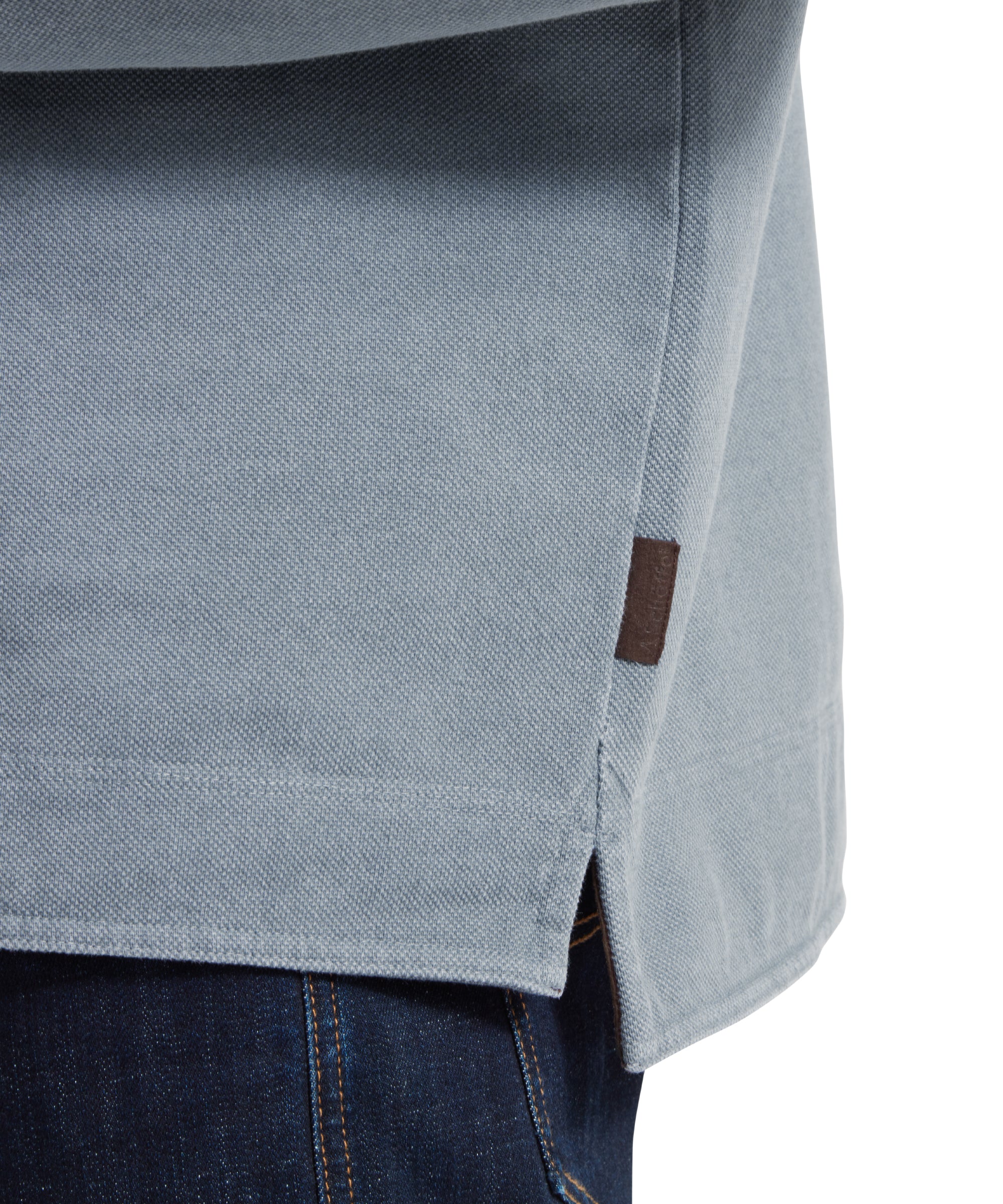 Close up image of a male model wearing a blue Schöffel sweatshirt with red shoulder and chest detailing and blue 'Schöffel countrywear' logo on the chest. It is paired with a red polo and dark denim jeans. Image highlights the split hem and pip tab.