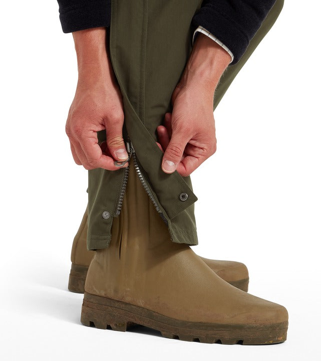 Close-up detail of the Schöffel Men's Ptarmigan Overtrouser in olive green, showing the ankle zip and button storm guard being fastened over rubber country boots