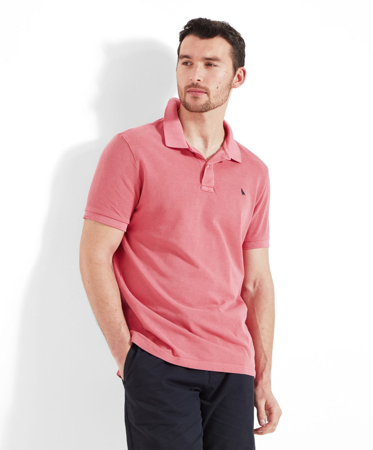 Man wearing coral pink short-sleeved garment dyed St Ives polo shirt with a black embroidered chest