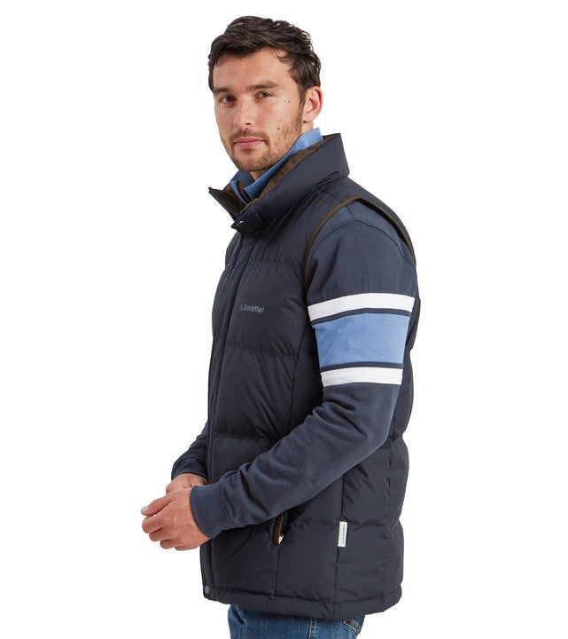 Male model wearing the Schöffel Men's Twickenham II Gilet in navy blue, shown from the side over a striped long-sleeve top and jeans