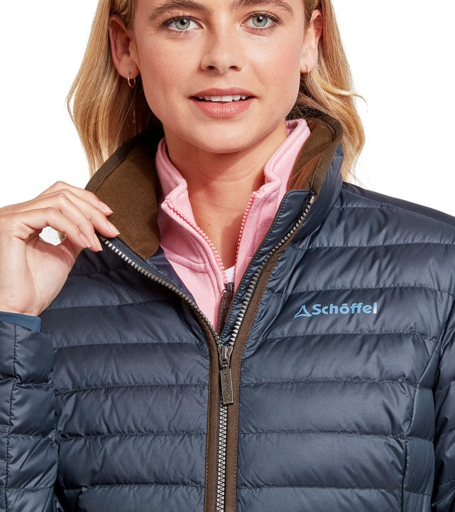 Woman wearing a navy puffer jacket with a visible Schöffel logo on a white background