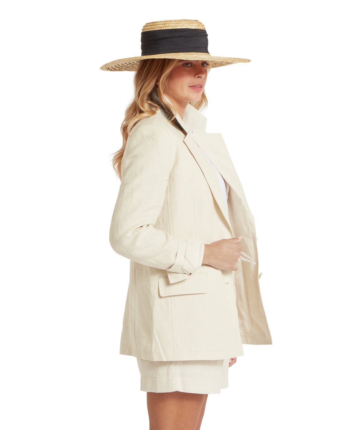 Woman wearing wide-brimmed straw hat with black ribbon and a henley linen blazer in oat color