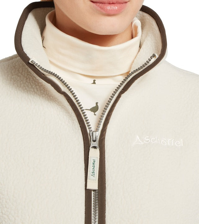 Schöffel Lyndon retro fleece gilet in white, close-up of textured sherpa fabric with contrast brown trim, full-length zip and embroidered logo, worn over pheasant-print roll neck