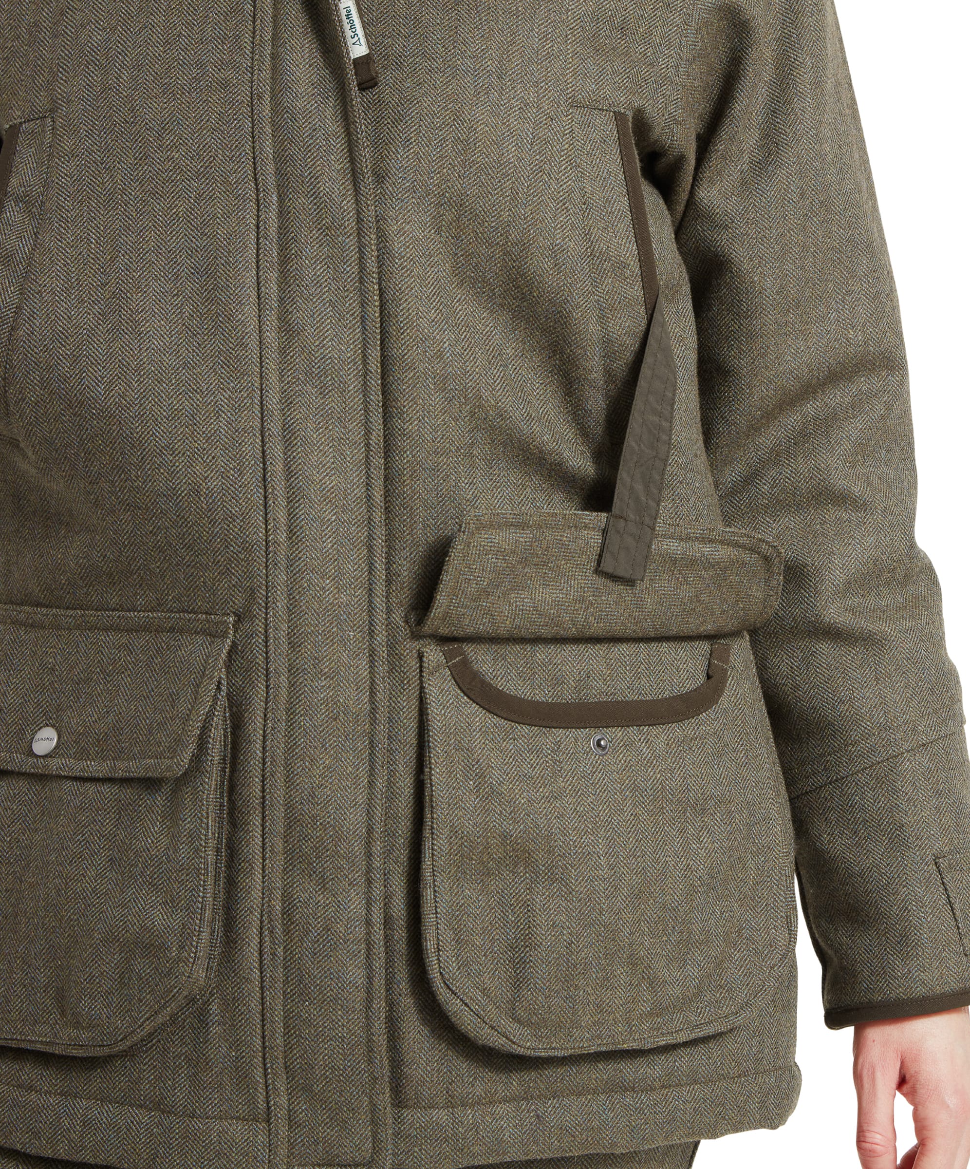 Close-up of the front pockets of a Schöffel Ptarmigan Tweed Coat for Women in Green, with one hand in the pocket, emphasising the practicality and detailing on the retainer strap.