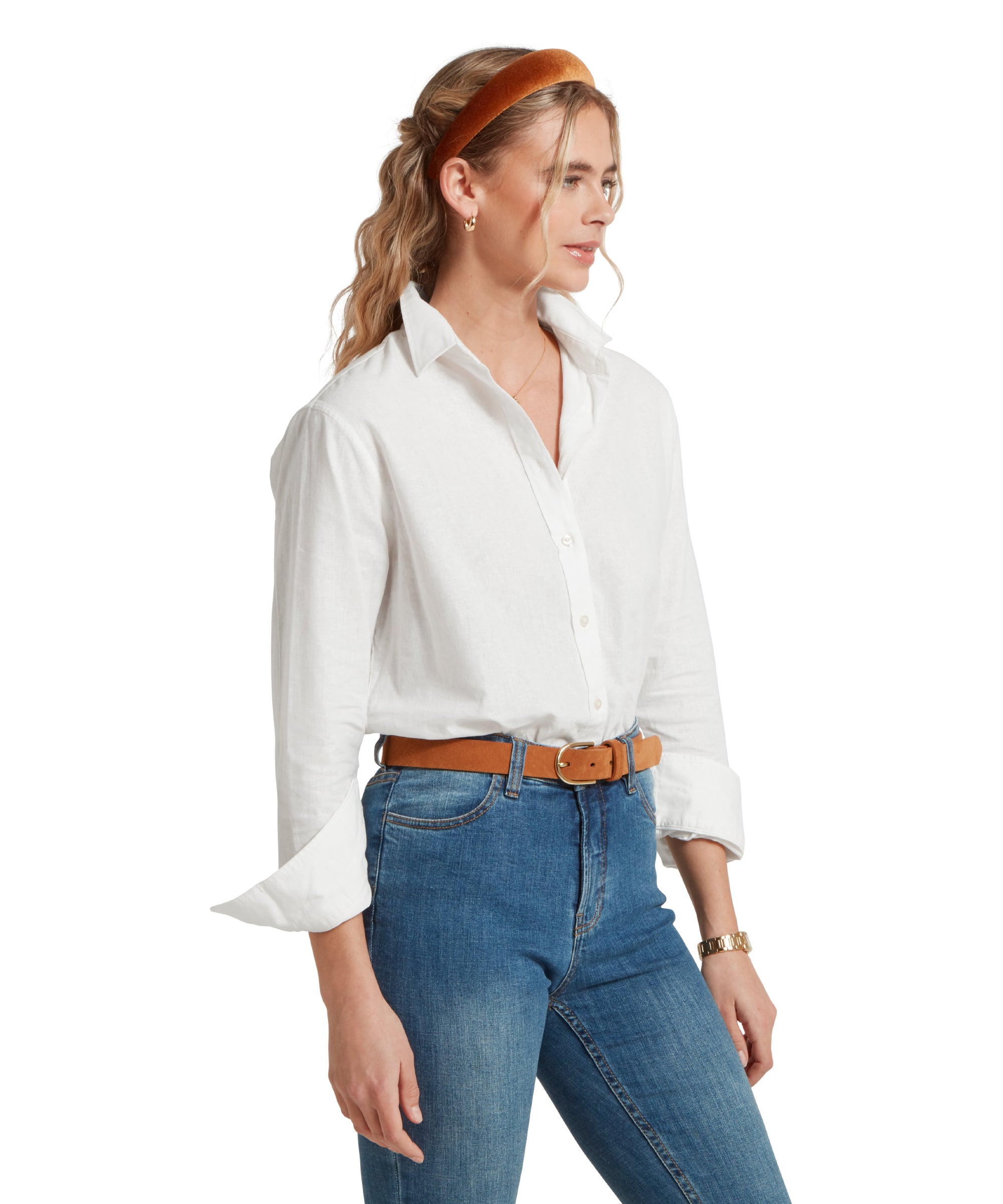 Side profile image of a female model wearing a tucked in white linen Schöffel shirt, paired with mid denim jeans, and tan leather belt. She is standing in a relaxed pose with her hands by her side.
