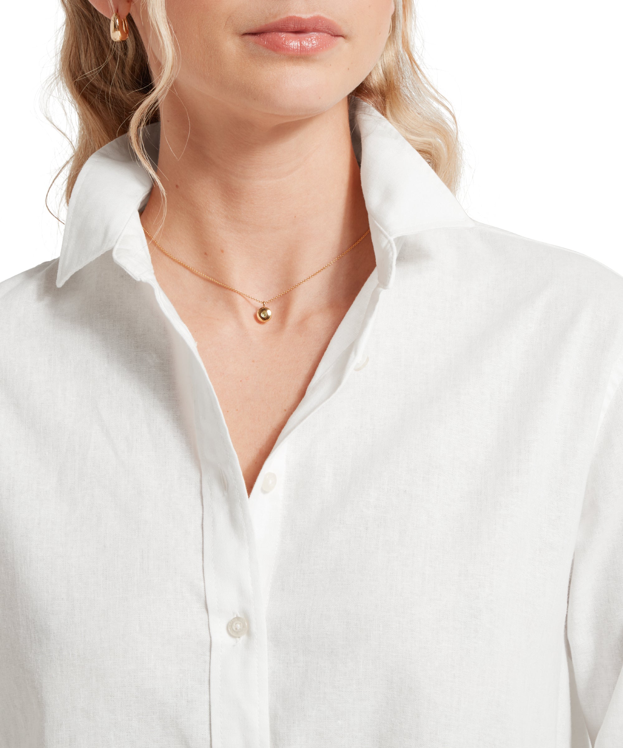 Close up image of a female model wearing a tucked in white linen Schöffel shirt paired with gold accessories. Image highlights the collar and button front. She is standing in a relaxed pose with one hands in her pocket.