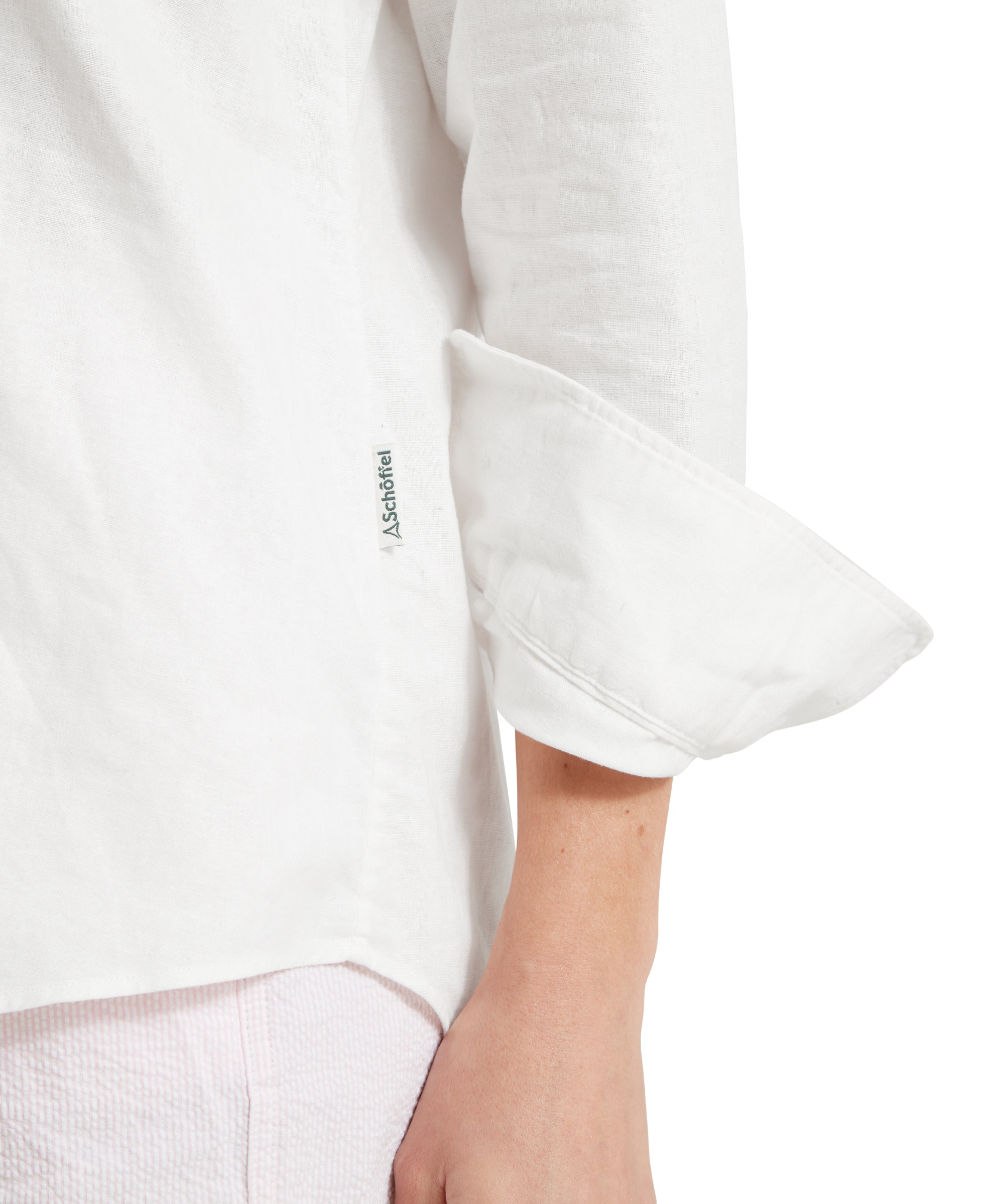 Close up image of a female model wearing a white linen Schöffel shirt, paired with light pink shorts. Image highlights the hem and "Schöffel" fabric side tag.