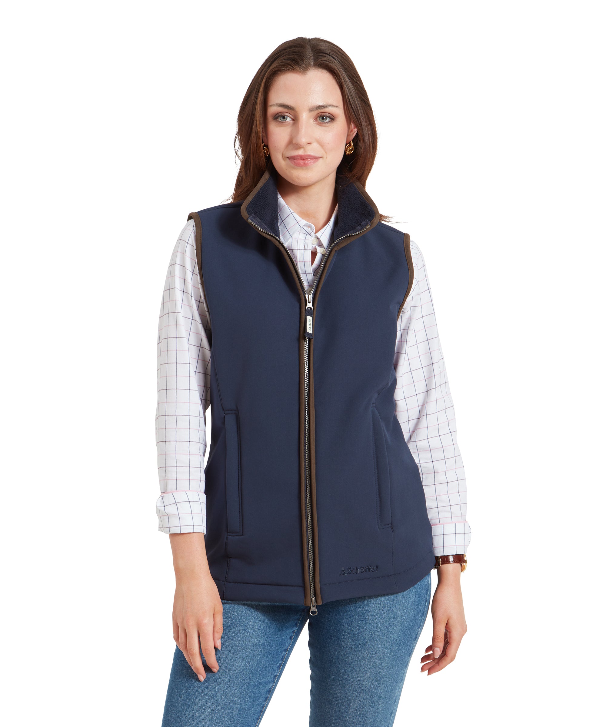 A woman wearing a Schöffel Belton Gilet for Women in Navy over a checkered shirt, standing with her hands in her pockets, smiling at the camera. The gilet has a high collar and a full-length zipper in the front.