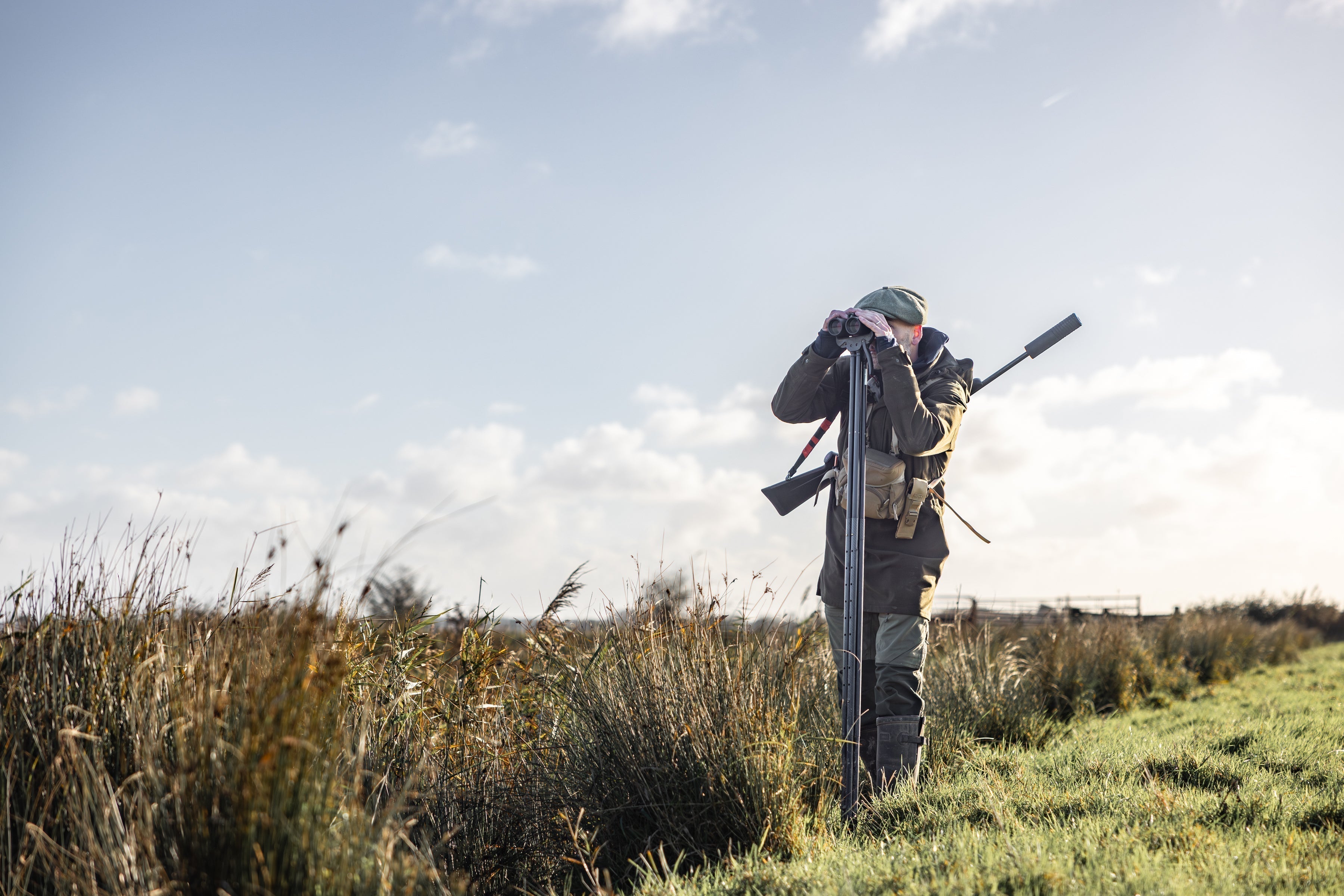 Hunter with double-barreled shotgun aims binoculars for wild venison hunt