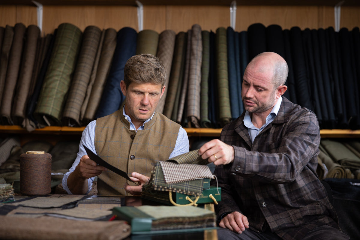 Two men sitting at a desk looking at tweed samples