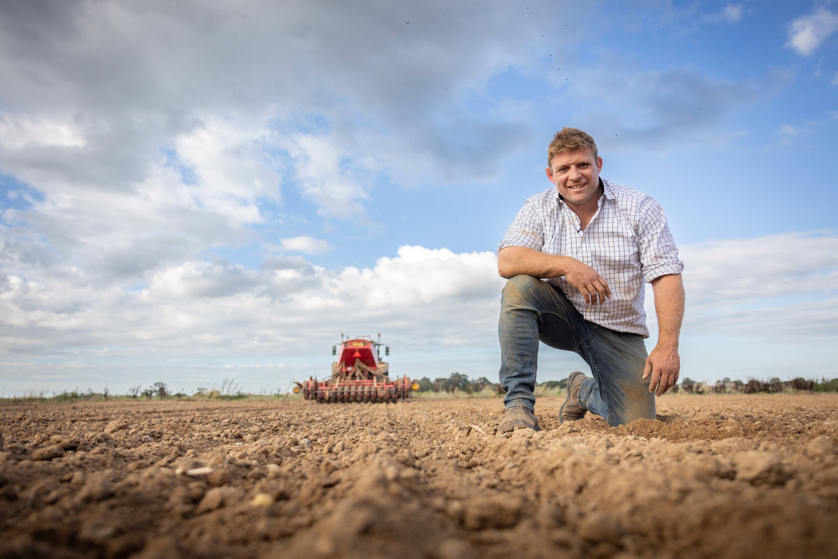 Tom Youngs kneeling in a freshly drilled field on his North Norfolk farm, a seed drill behind him