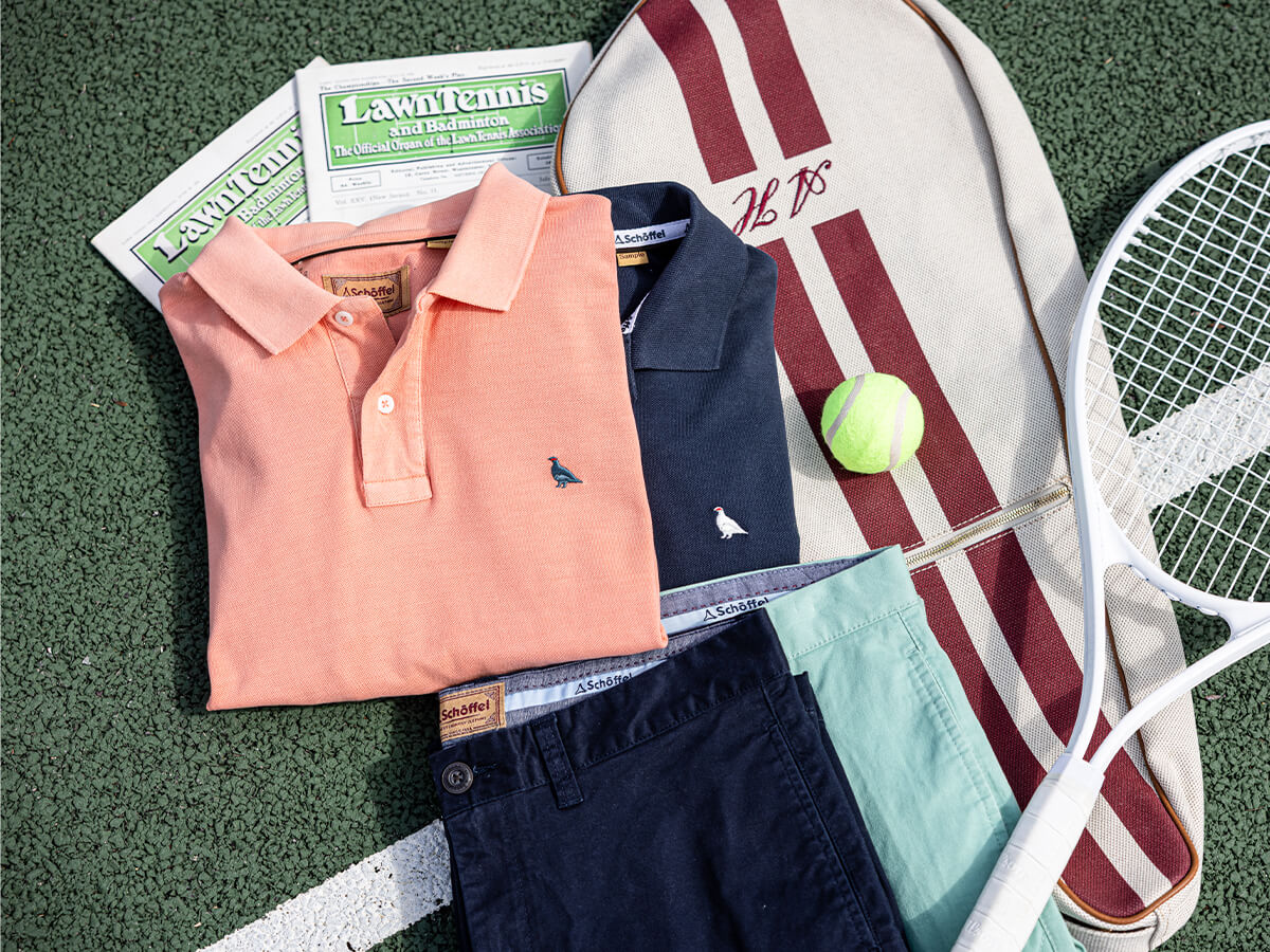 Collection of polo shirts, shorts, and a tennis racket on a tennis court surface.