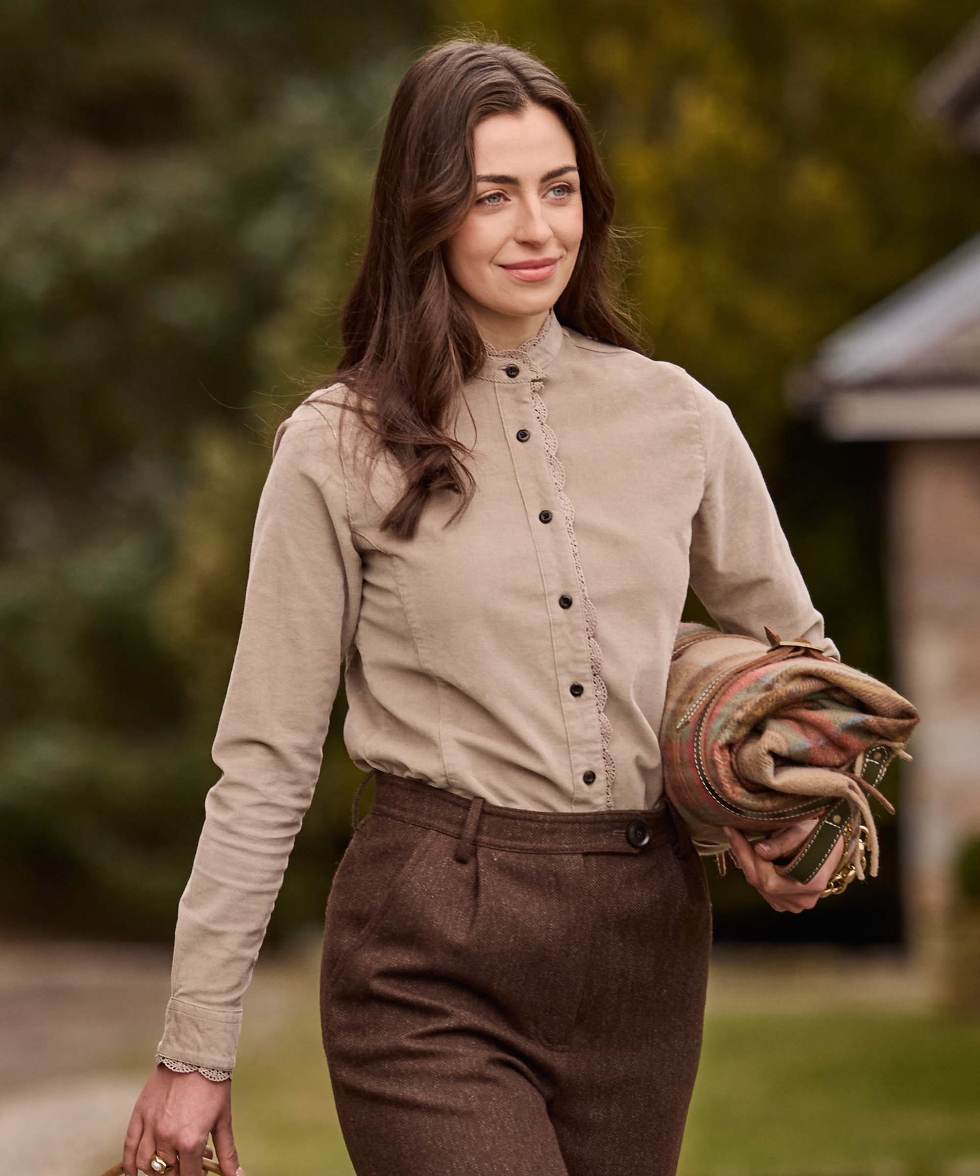 Woman walking outdoors in a taupe cotton corduroy shirt with delicate lace trim, paired with brown herringbone tweed trousers – timeless Schöffel Country tailoring