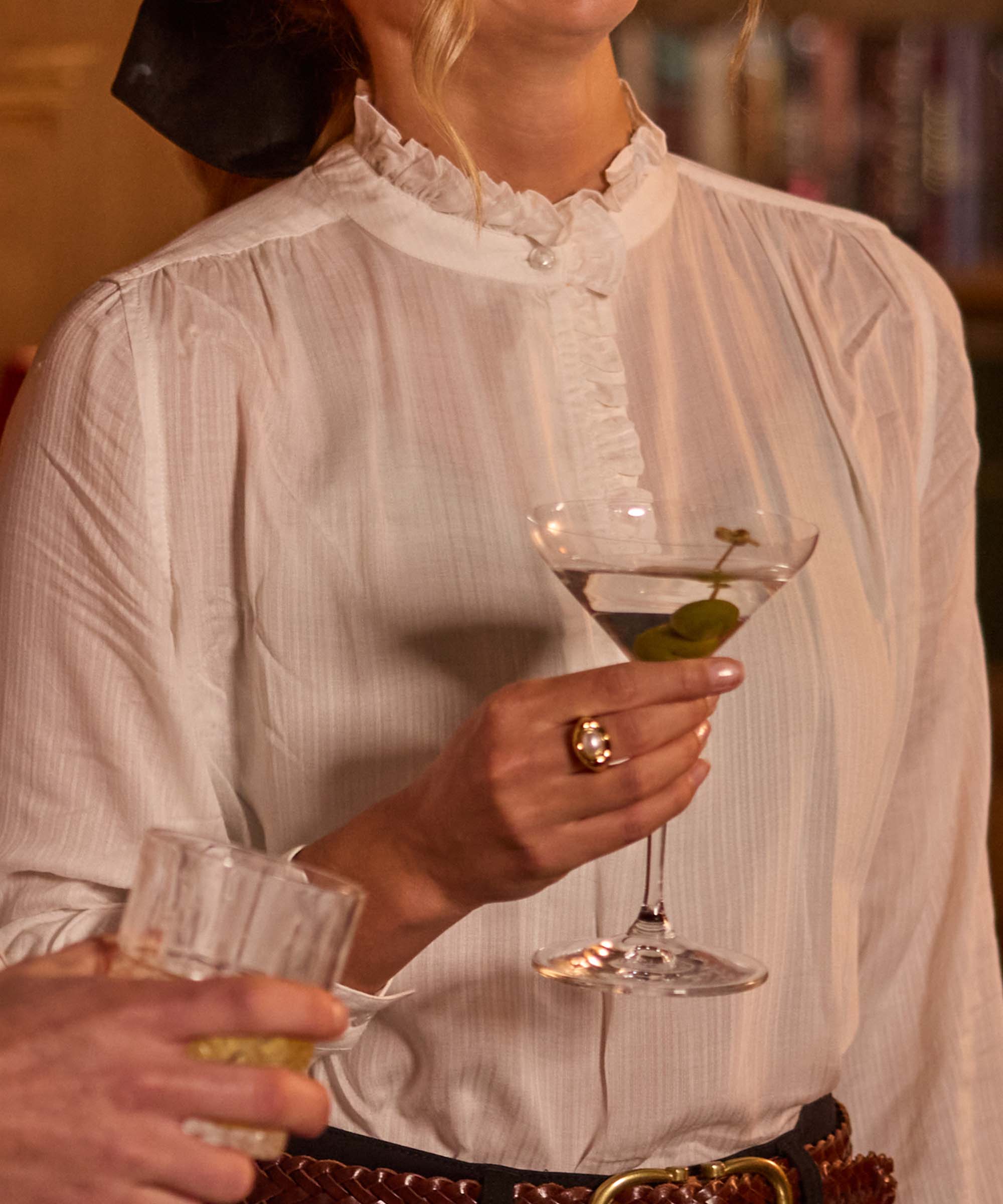 Close-up of a white cotton blouse with a delicate ruffled collar and mother-of-pearl style button, finished with a woven leather belt