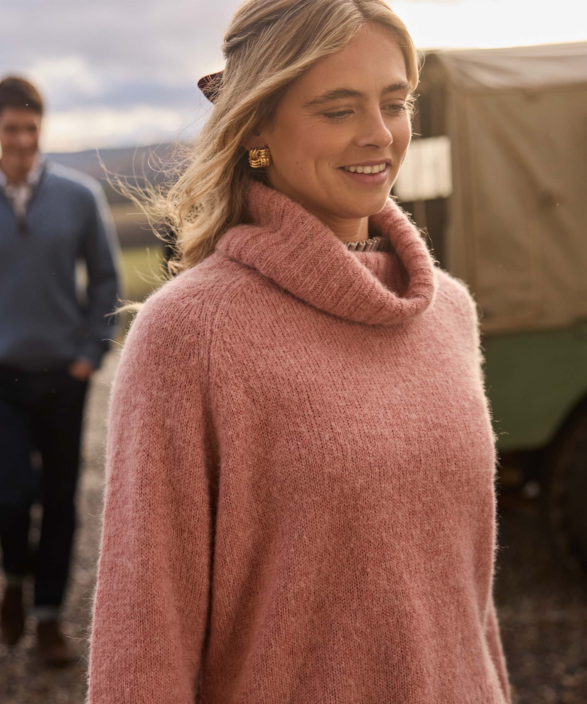 Close-up of a woman in a soft pink cowl neck knit jumper, highlighting the relaxed roll neck and chunky yarn