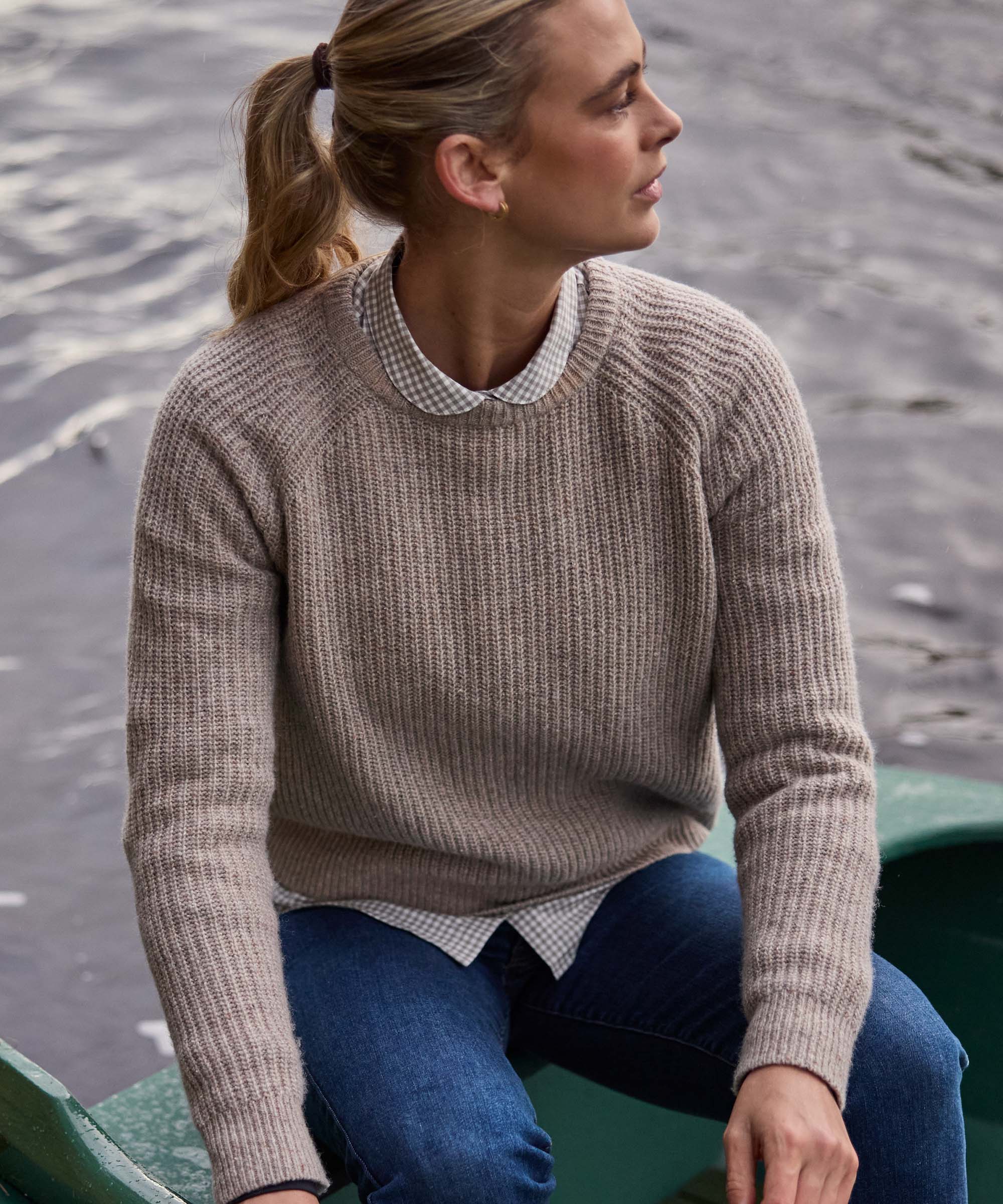 Woman in a rowing boat wearing an oatmeal ribbed jumper over a gingham shirt, classic Schöffel Country layering for the outdoors