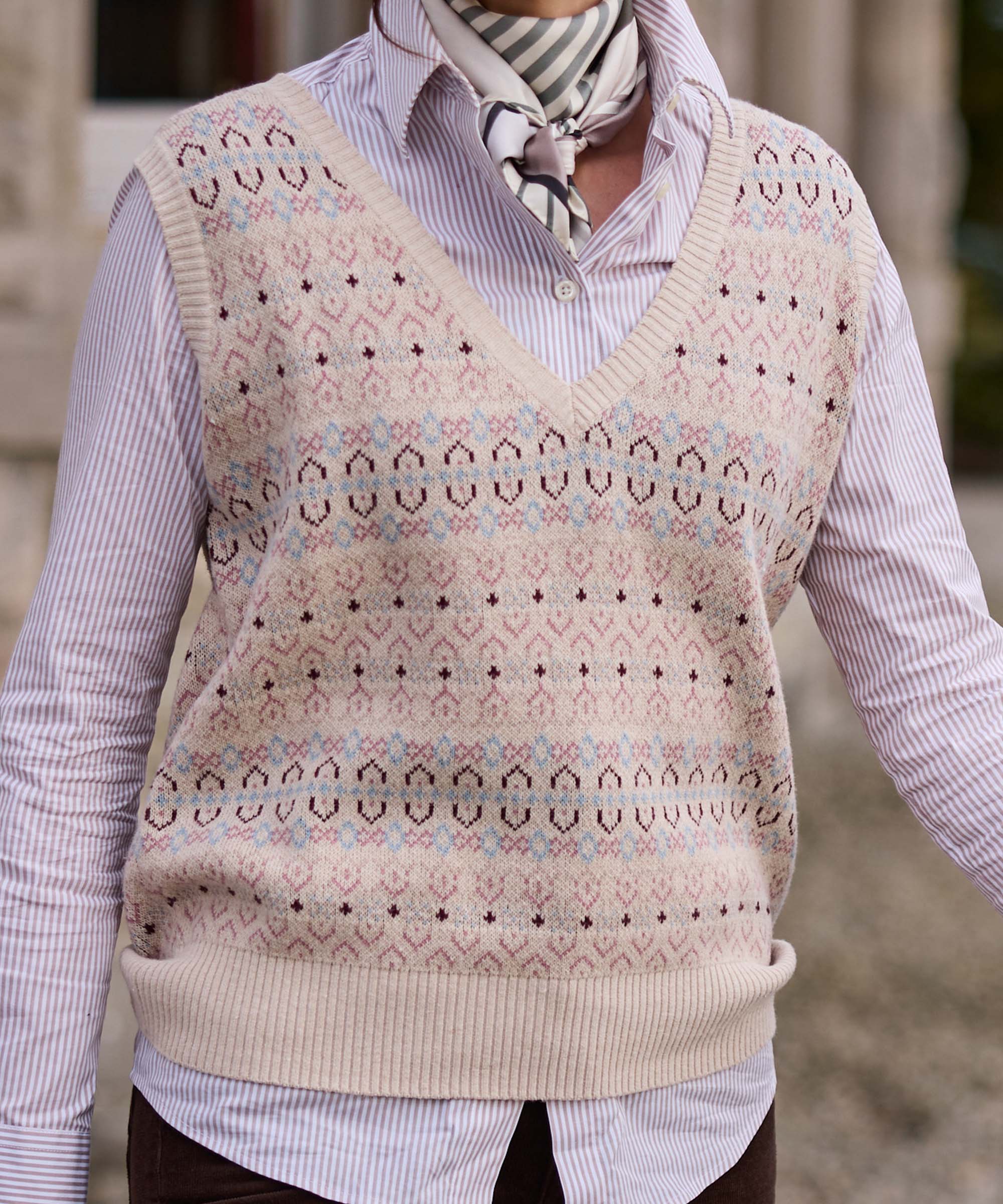 Close-up of a cream Fair Isle knitted tank worn over a pink striped shirt with a silk neck scarf – heritage patterned knitwear from Schöffel Country