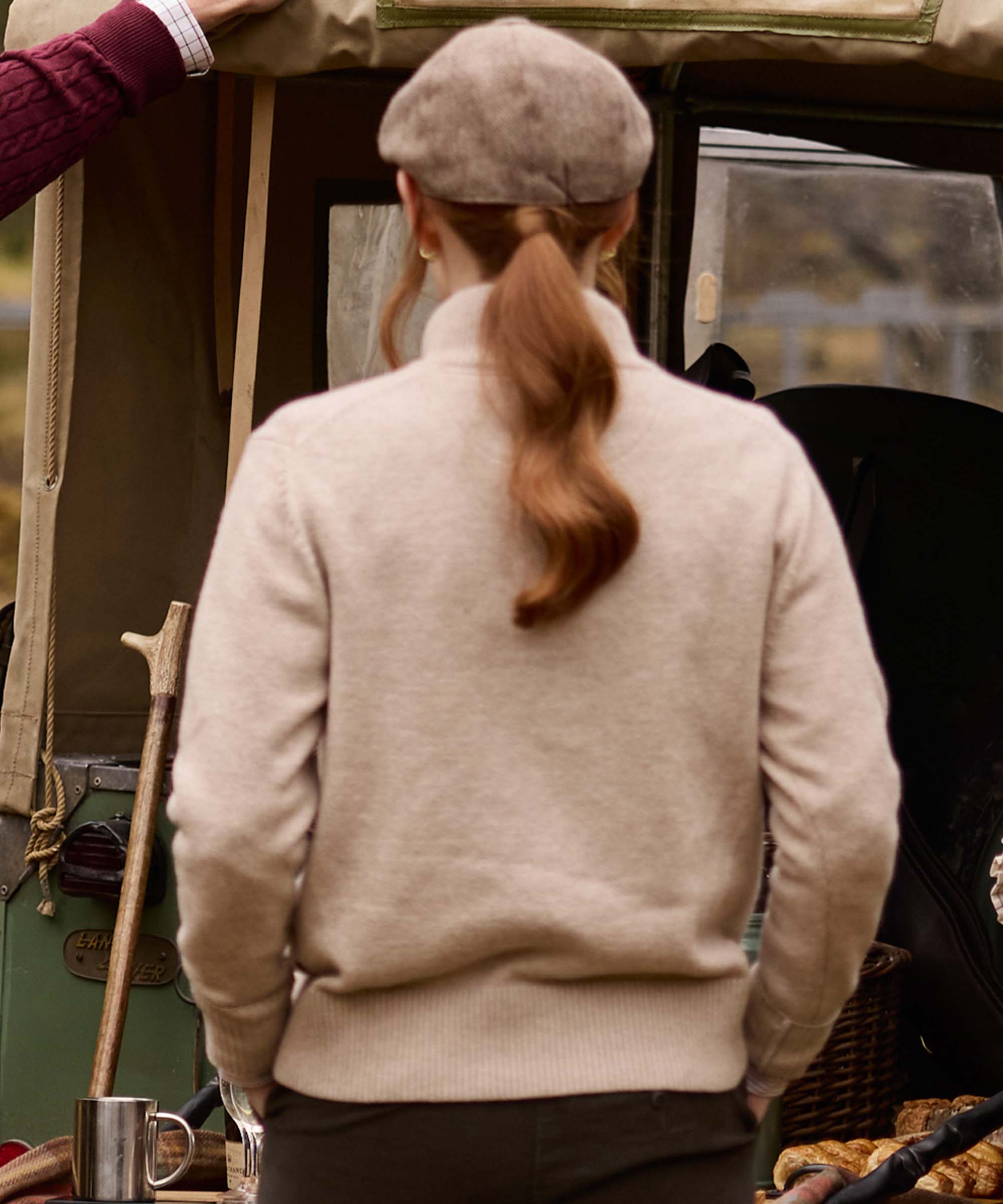 Close-up from behind of an oatmeal quarter-zip jumper and herringbone flat cap, showing the ribbed hem and relaxed fit