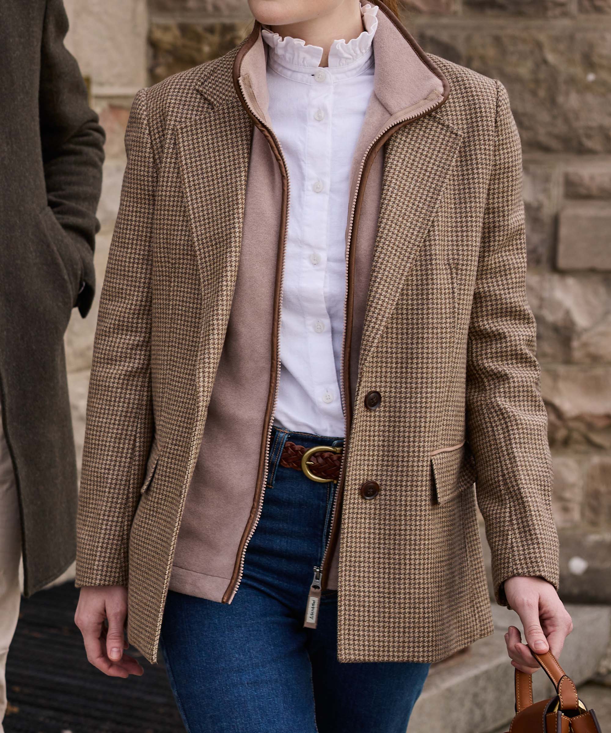 Close-up of a houndstooth tweed jacket with tan suede collar and leather piping, layered over a white ruffle-neck blouse