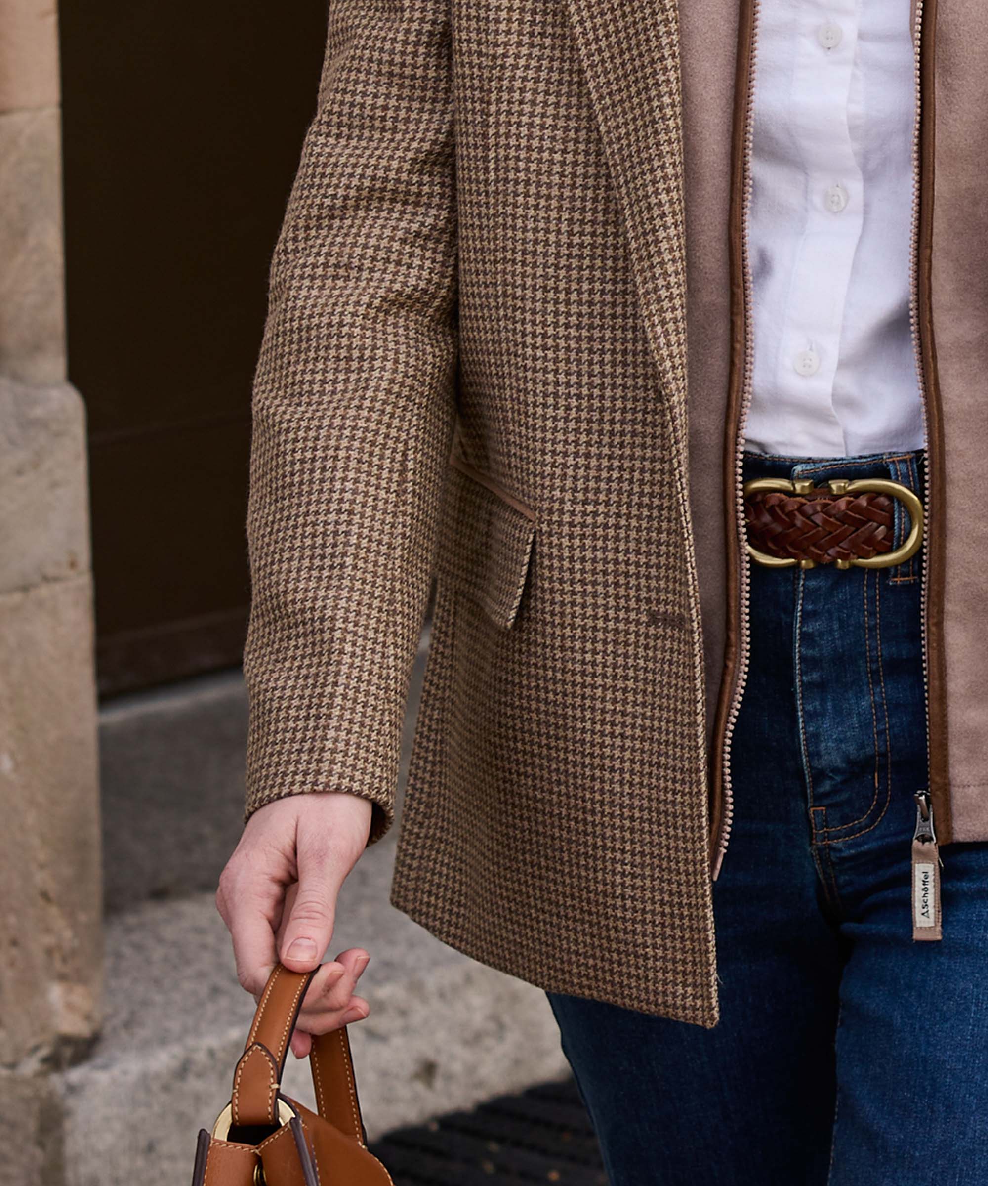 Detail of a houndstooth tweed jacket sleeve with leather-trimmed pocket, styled with a woven leather belt and denim
