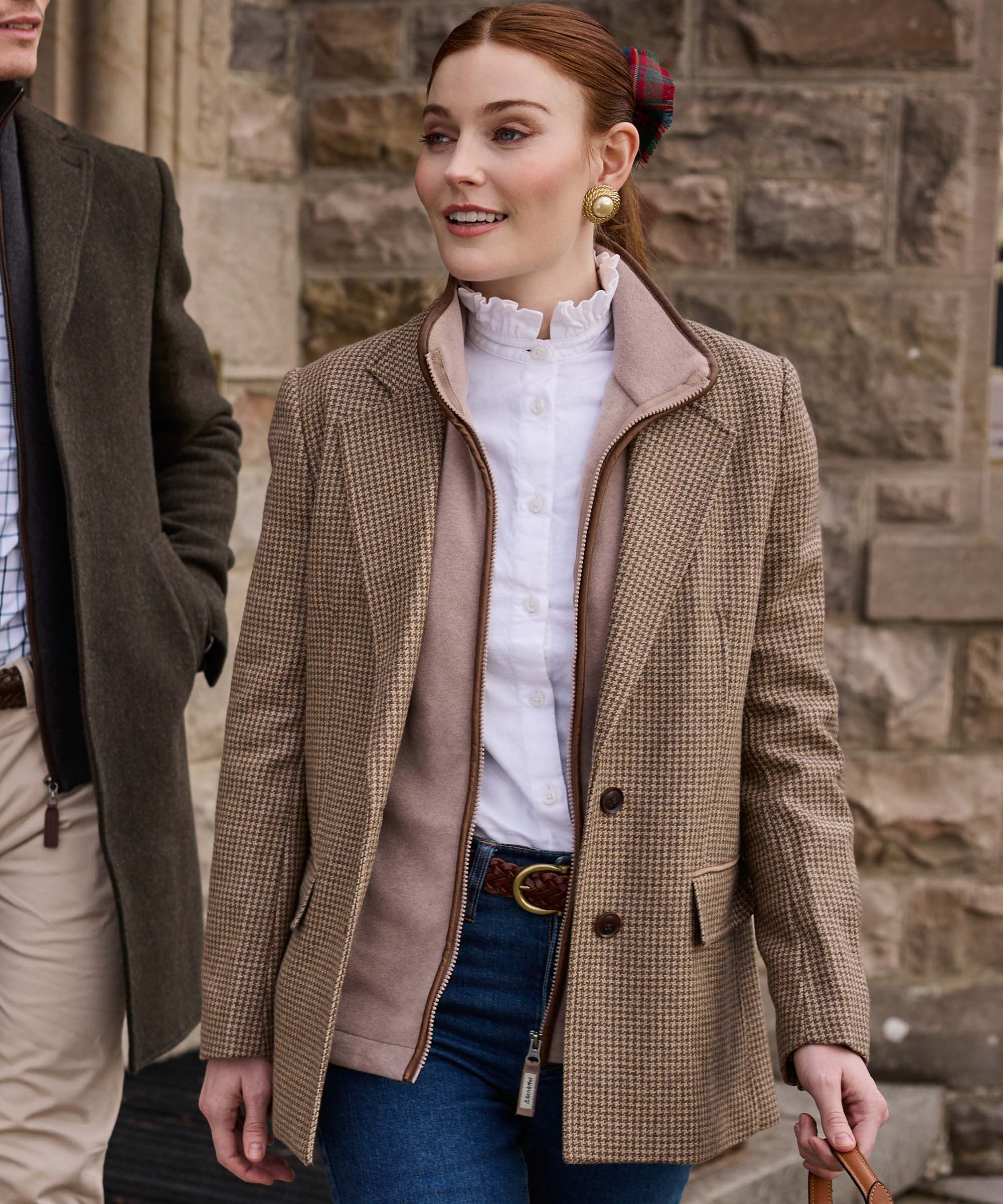 Woman in a houndstooth tweed jacket with contrast suede collar and leather trim, worn over a ruffle-neck blouse and jeans