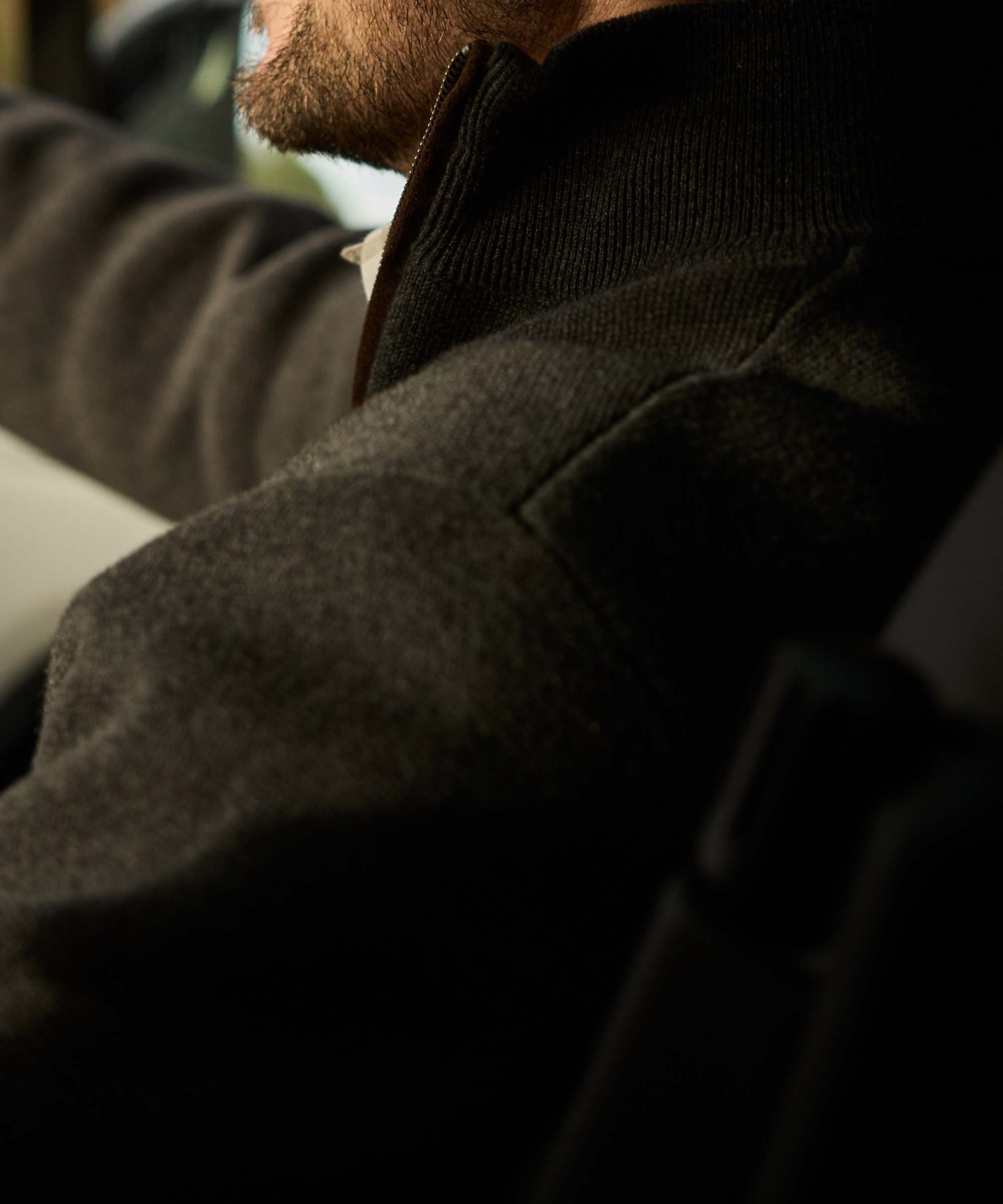 Close-up of a charcoal quarter-zip jumper collar and leather-trimmed zip, layered over a check shirt
