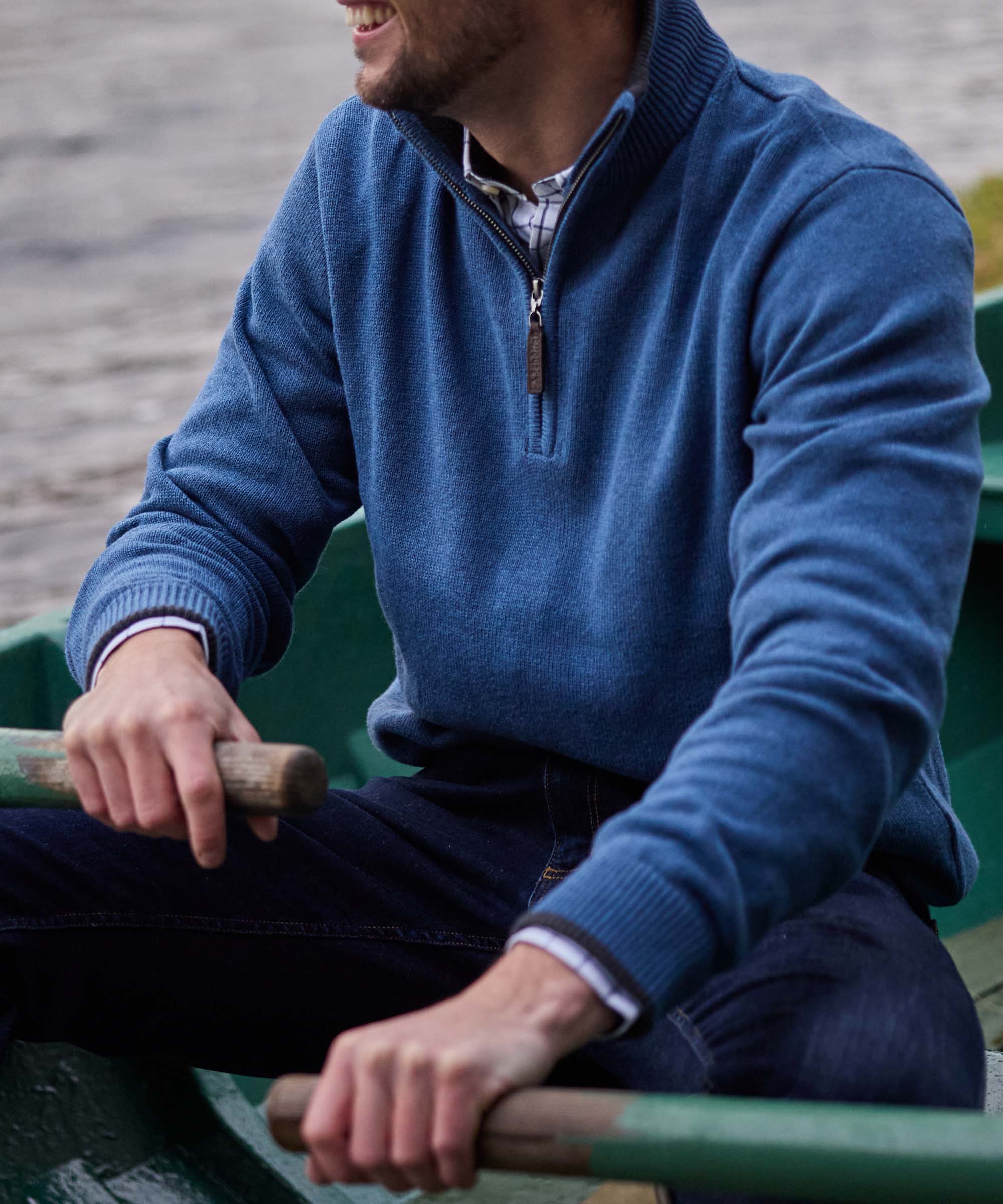 Close-up of a man rowing in a denim-blue quarter-zip jumper, showing the ribbed collar and leather zip pull