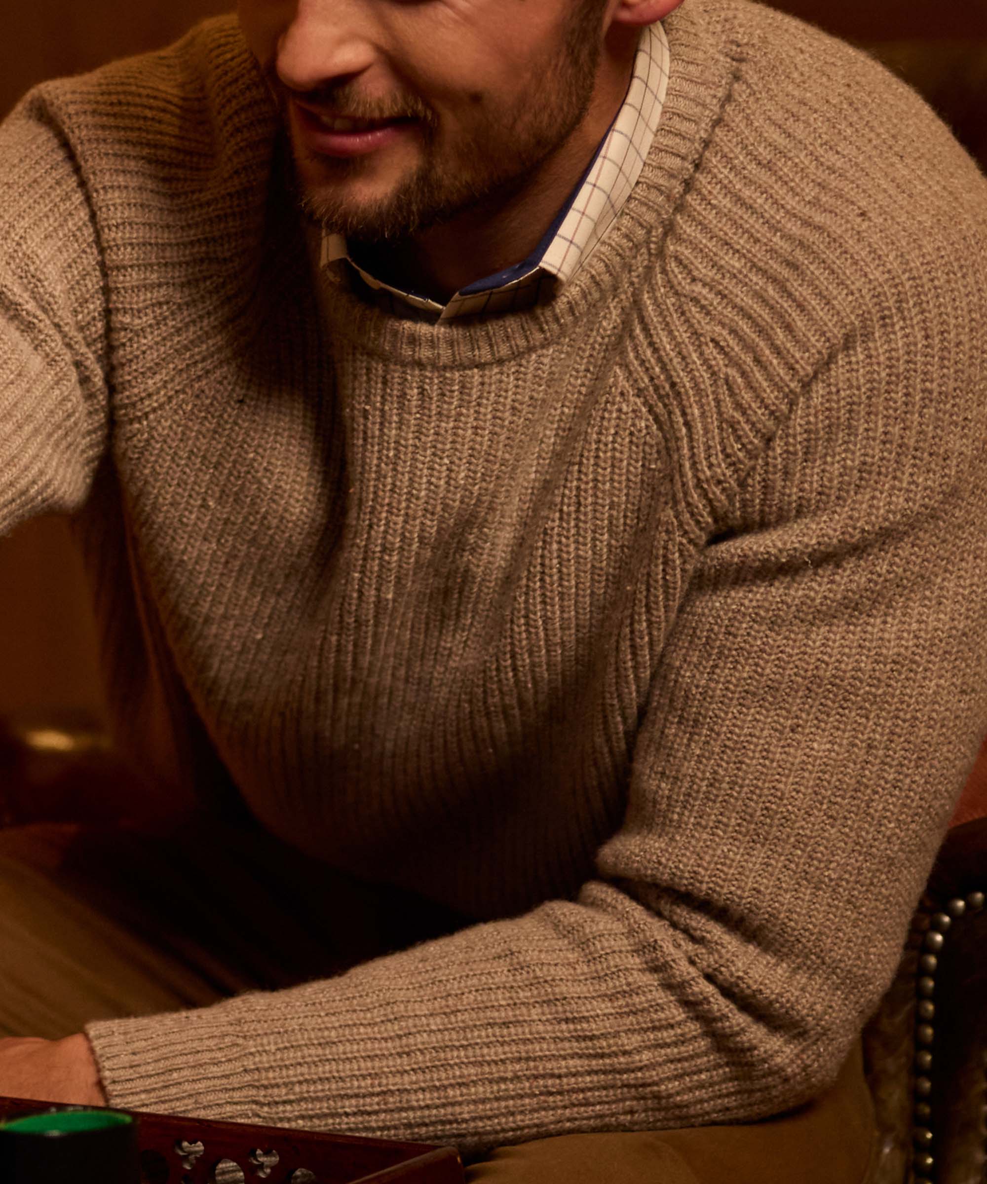 Close-up of an oatmeal ribbed crew neck jumper, showing the chunky knit texture over a check shirt collar