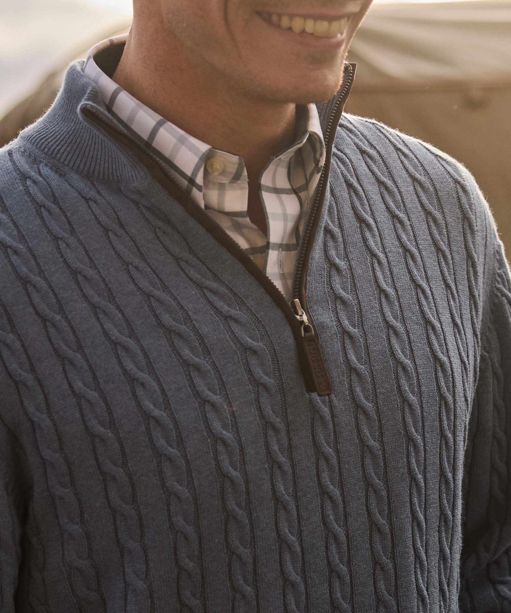 Close-up of a dip-dyed blue cable knit quarter-zip jumper collar and zip, worn over a check shirt