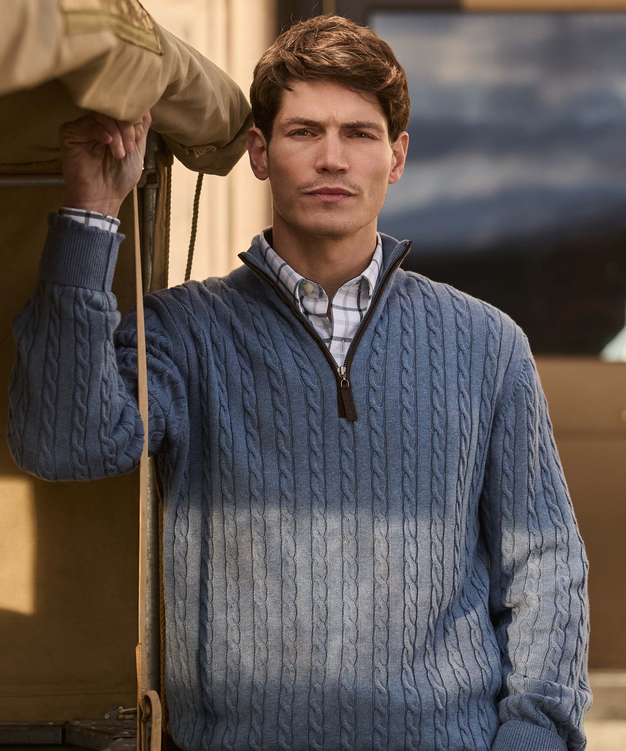Man standing outdoors in a dip-dyed blue cable knit quarter-zip jumper, layered over a check shirt