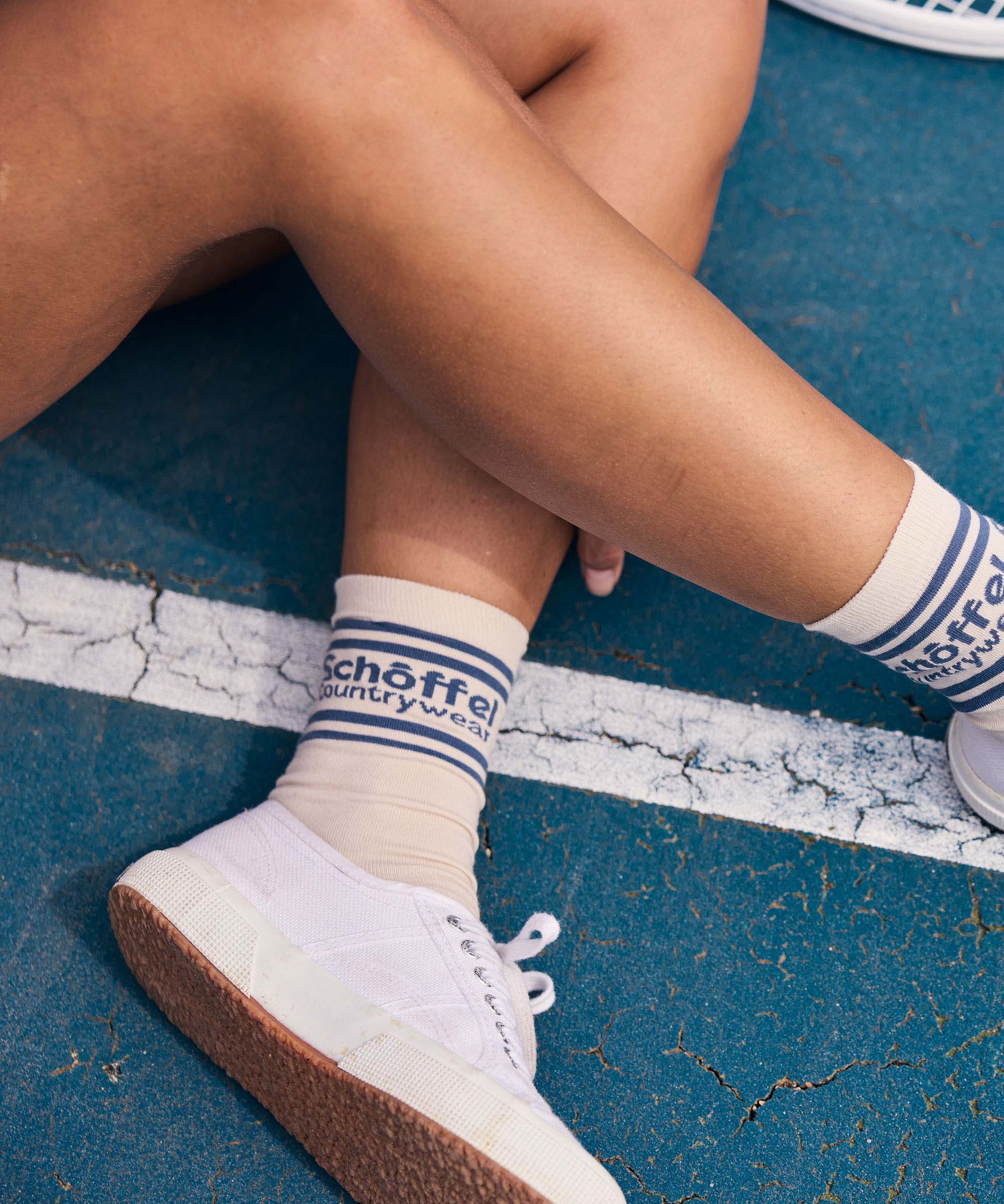 Person wearing white sneakers with blue soles and striped socks on a blue surface.
