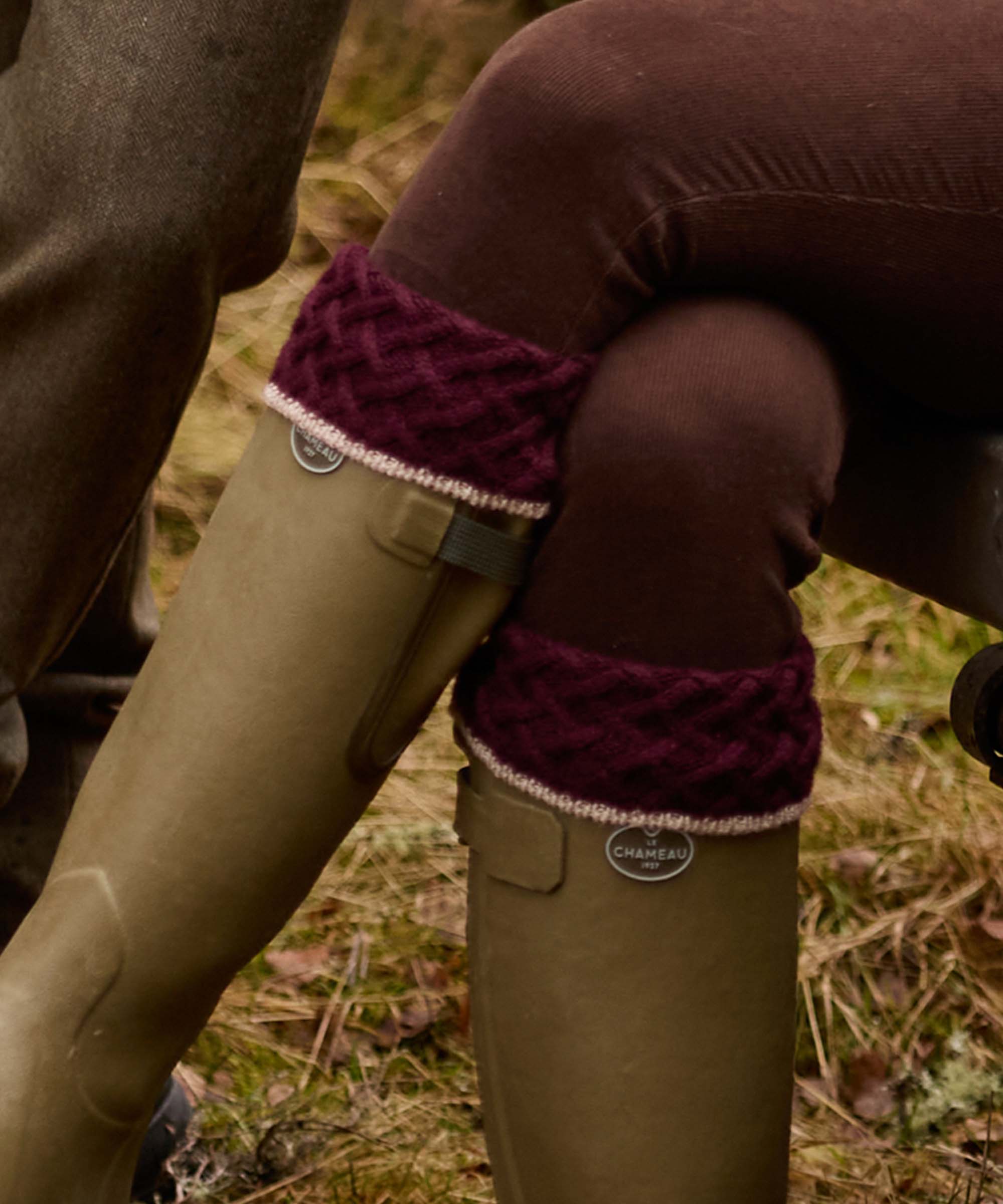 Close-up of a burgundy cable knit sock garter tucked into a Le Chameau wellington boot, worn with tweed breeks