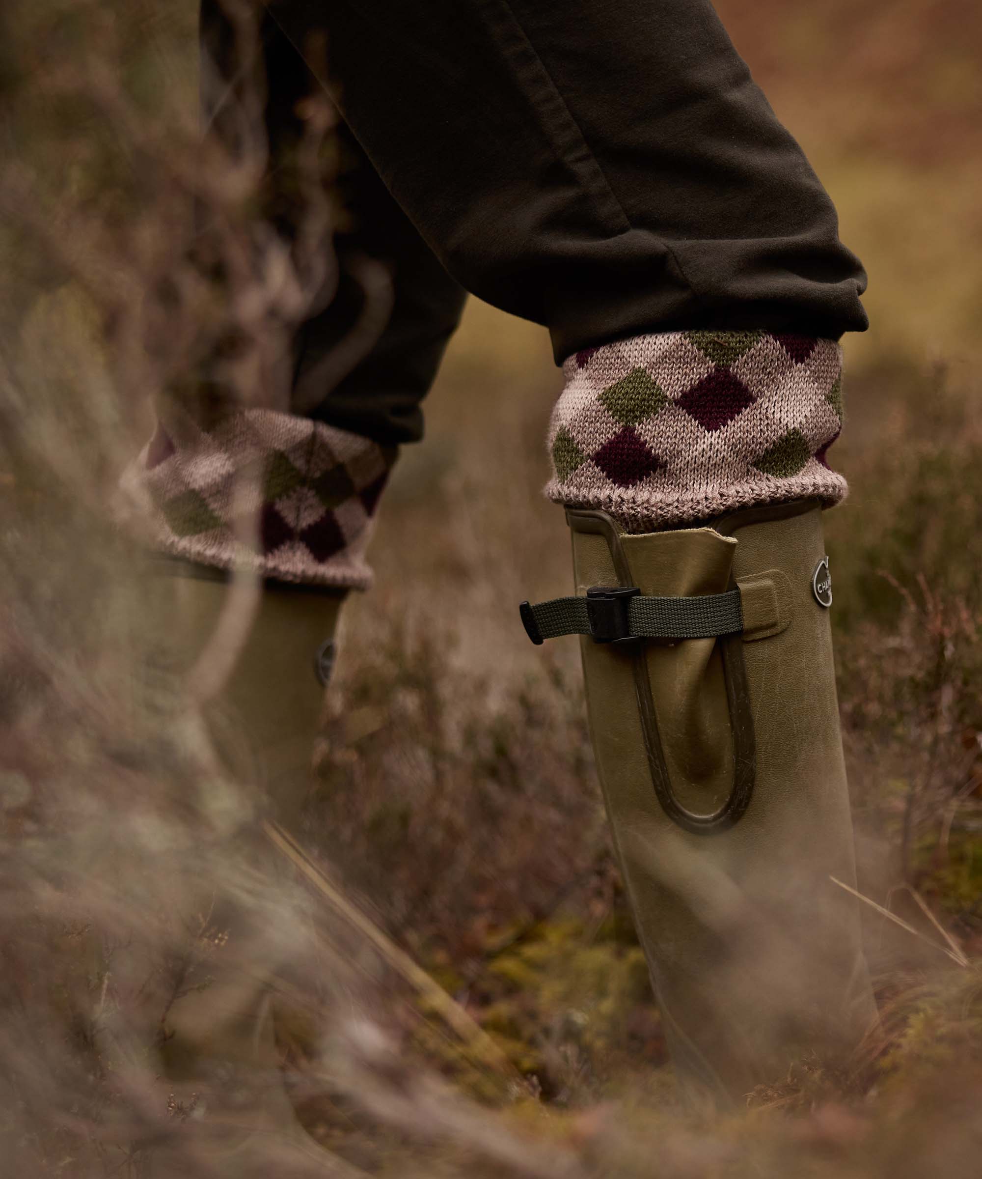 Close-up of matching diamond-patterned sock garters worn with wellington boots, walking through autumn heather