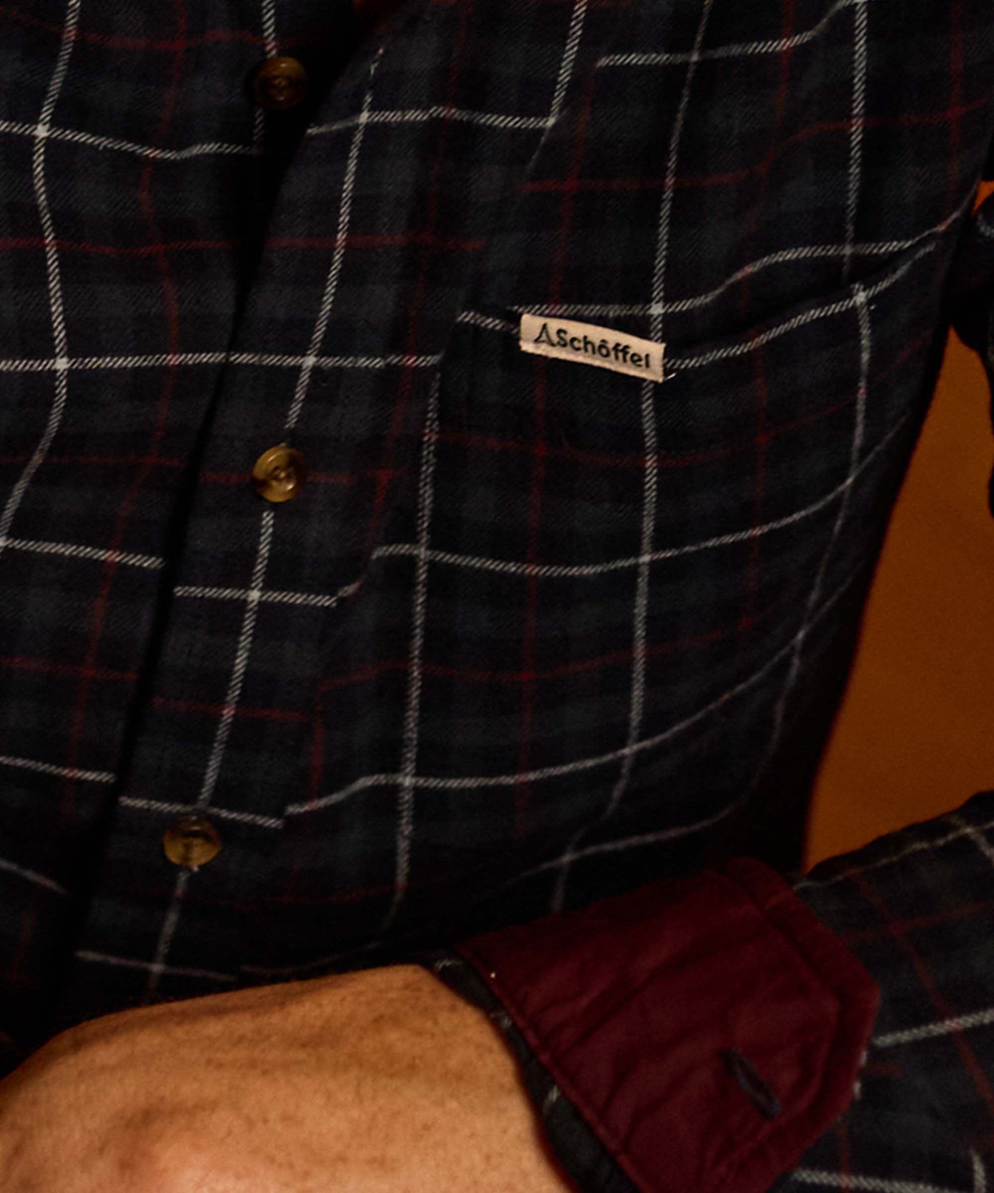 Close-up of a navy check flannel shirt's Schöffel label and burgundy contrast cuff