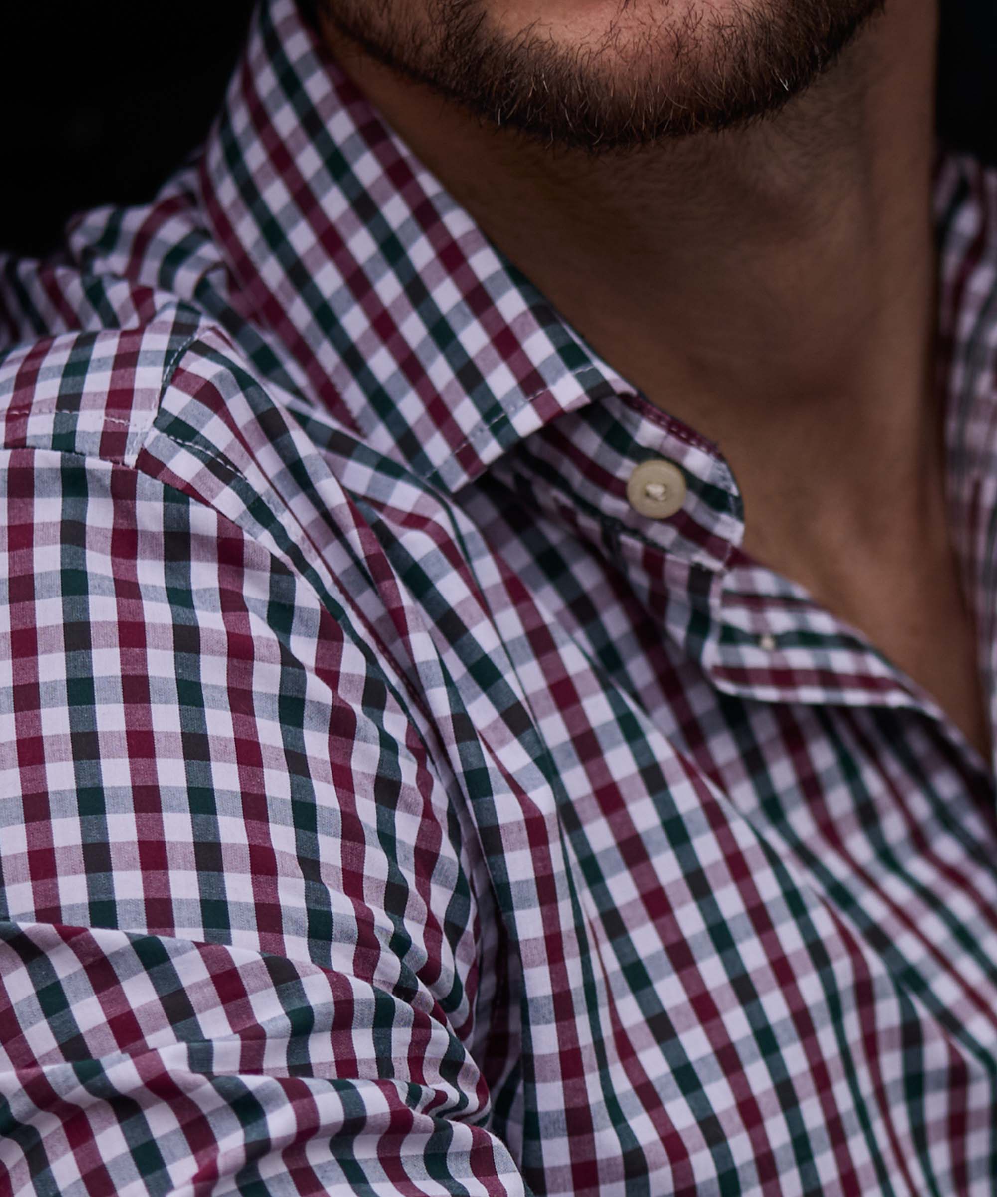 Close-up of a burgundy, green and white gingham check shirt collar and button detail