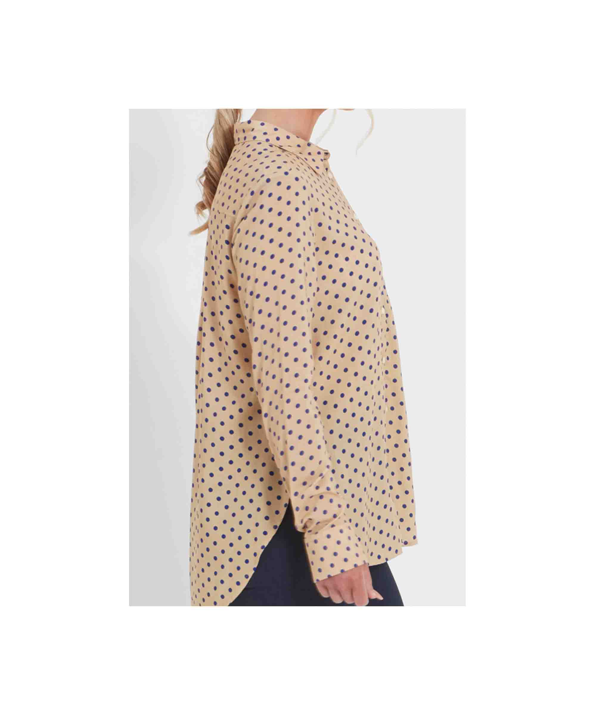 Beige polka dot blouse worn by a person on a white background