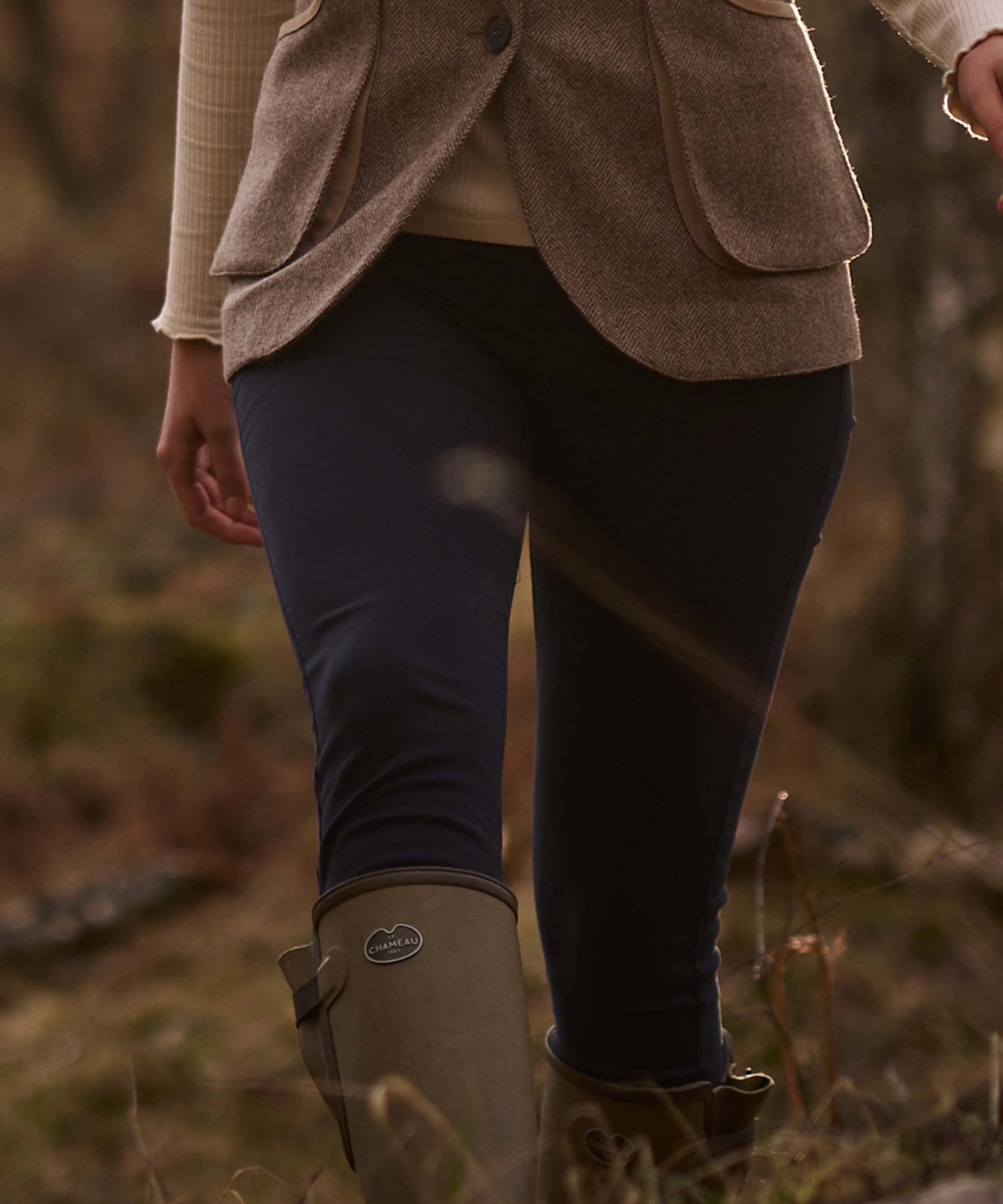 Close-up of navy technical riding trousers worn beneath a tweed jacket, tucked into Le Chameau wellington boots