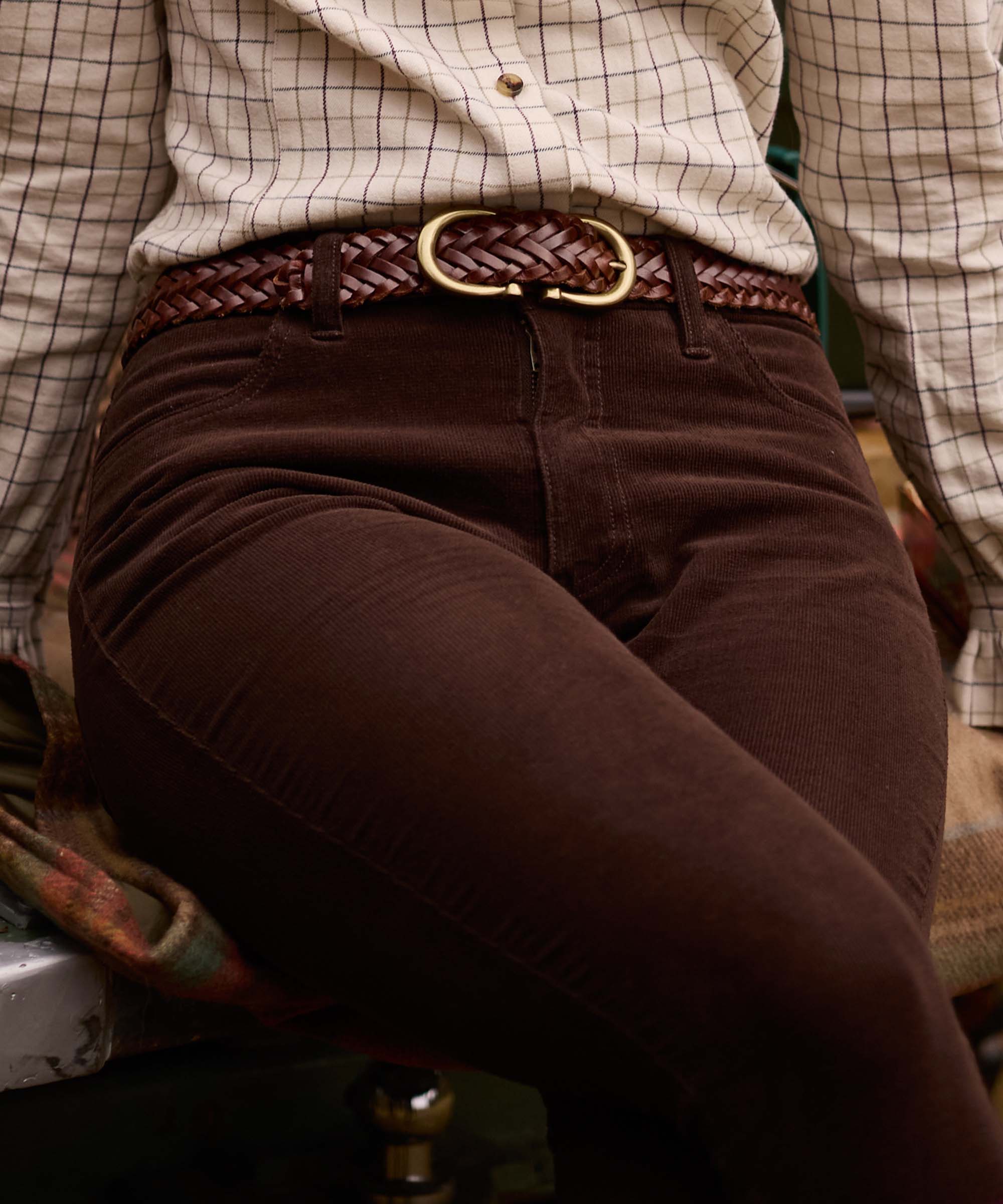 Close-up of Schöffel Country's brown corduroy trousers styled with a plaited leather belt and check shirt