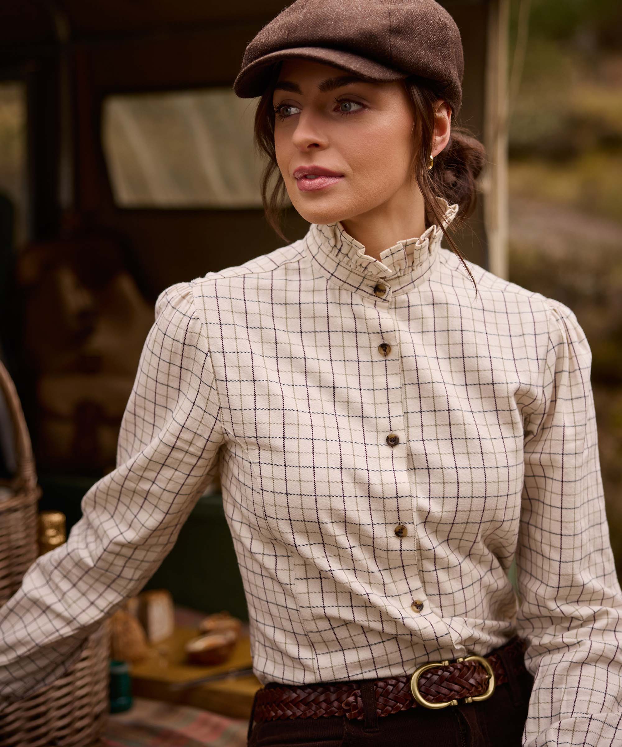 Close-up of woman in flat cap wearing Schöffel Country's ivory check ruffle-neck shirt, styled with a plaited leather belt