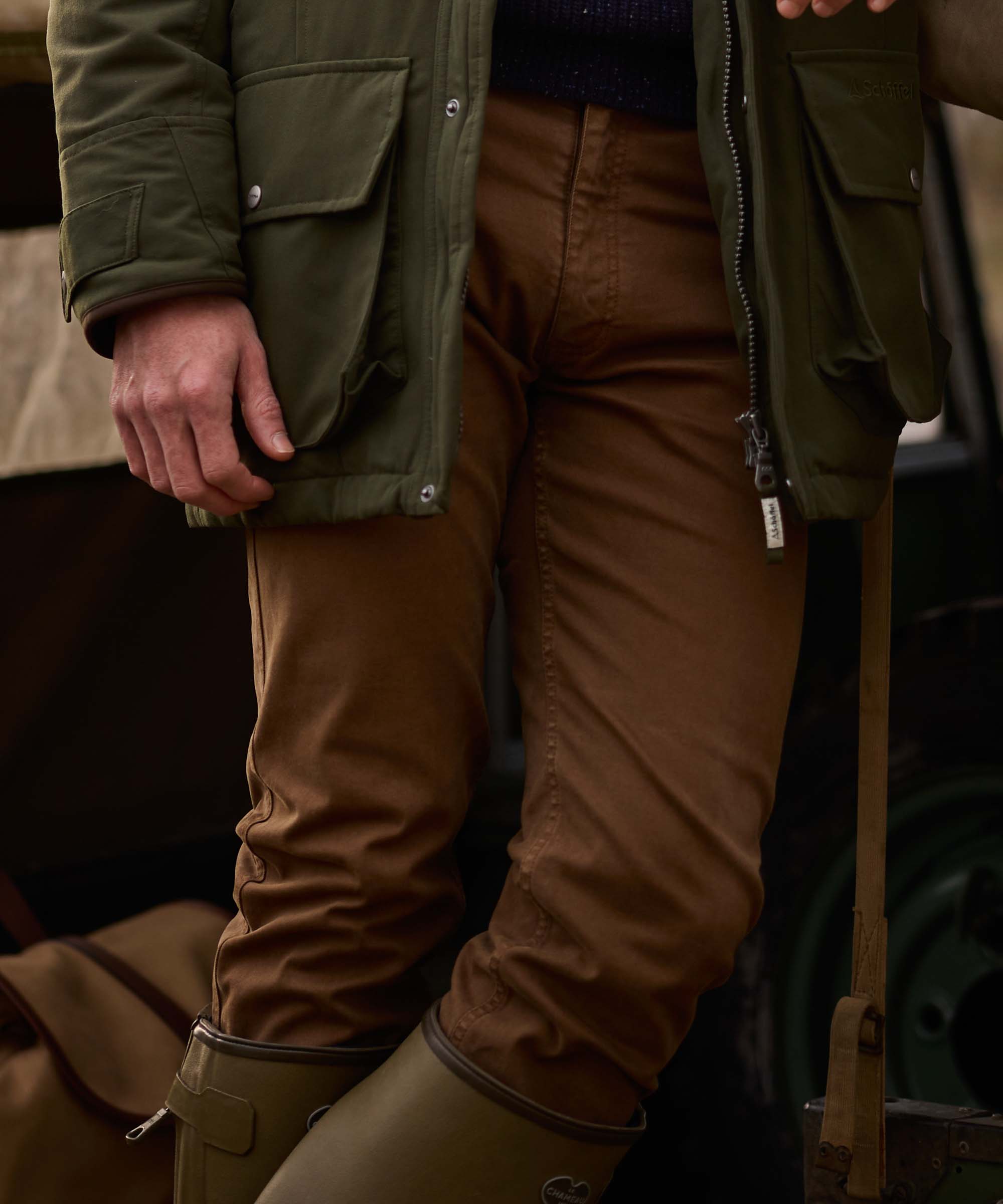 Man wearing Schöffel Country's tan cotton trousers with an olive quilted field jacket, hand resting in pocket